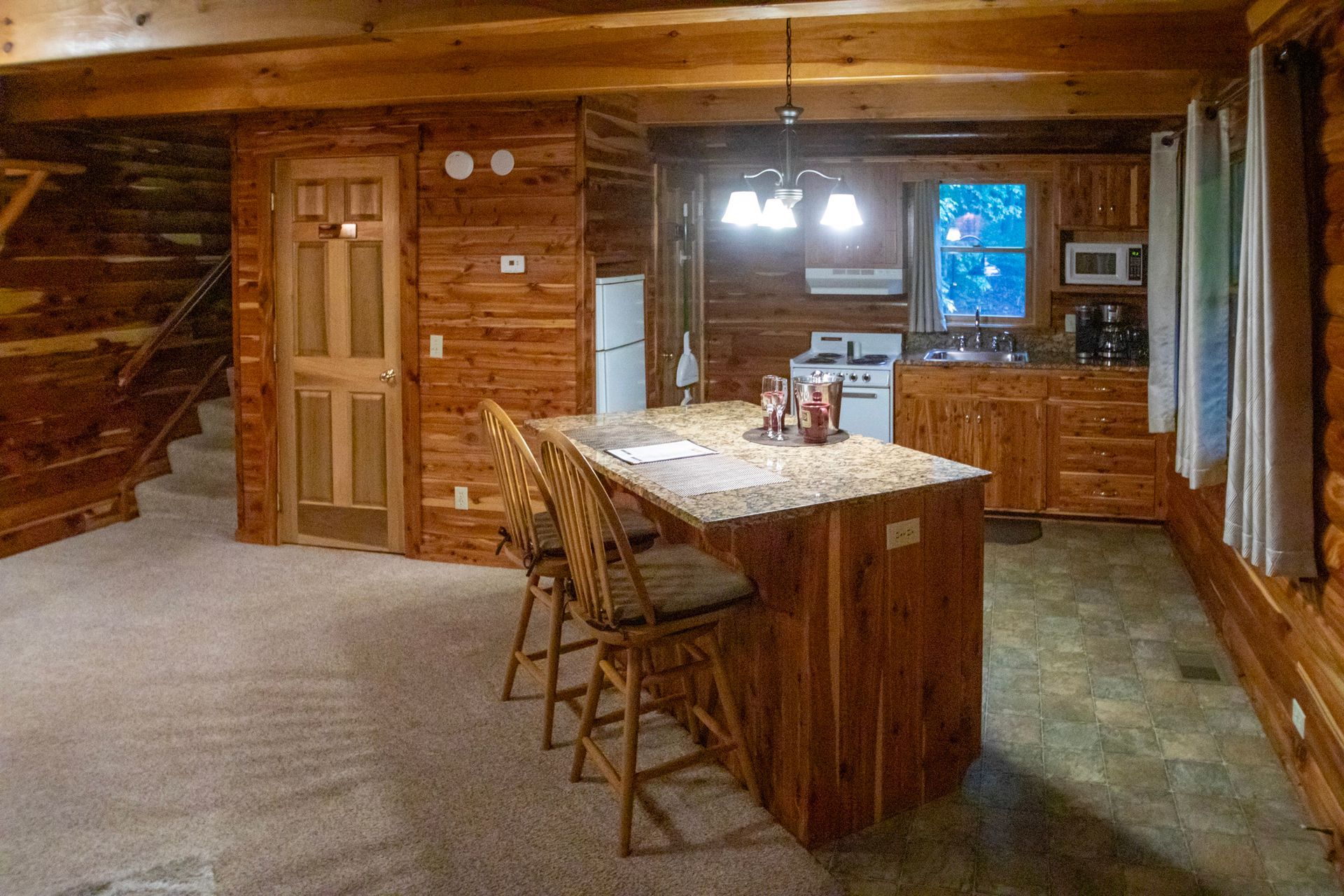 Log cabin interior with a kitchen island and bar stools, wooden walls, and a staircase.