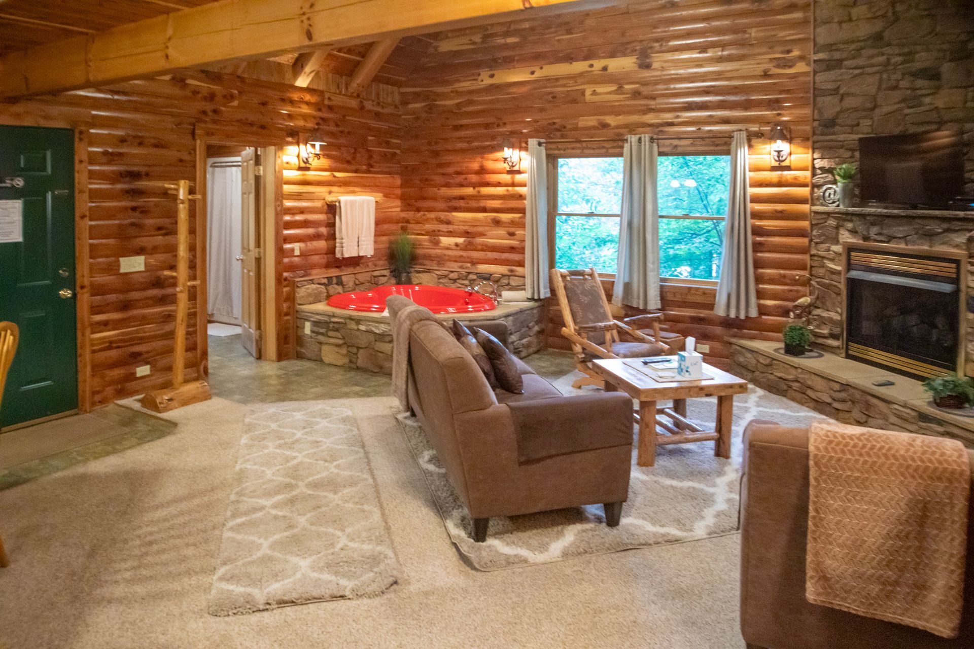 Cozy cabin living room with fireplace, hot tub, and sofa. Wooden walls and natural light.