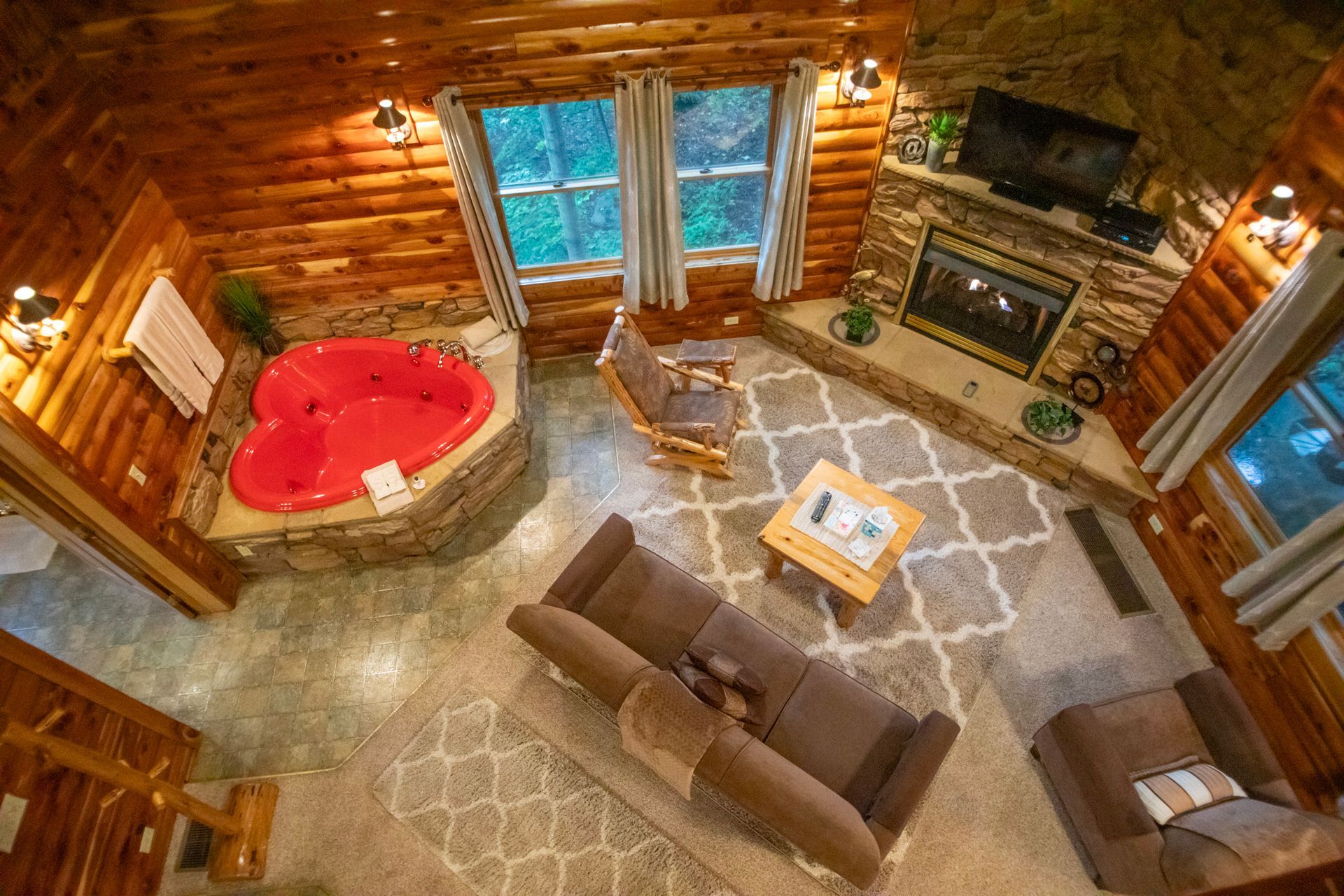 Cozy cabin interior, featuring a red heart-shaped hot tub, fireplace, sofa, and windows.