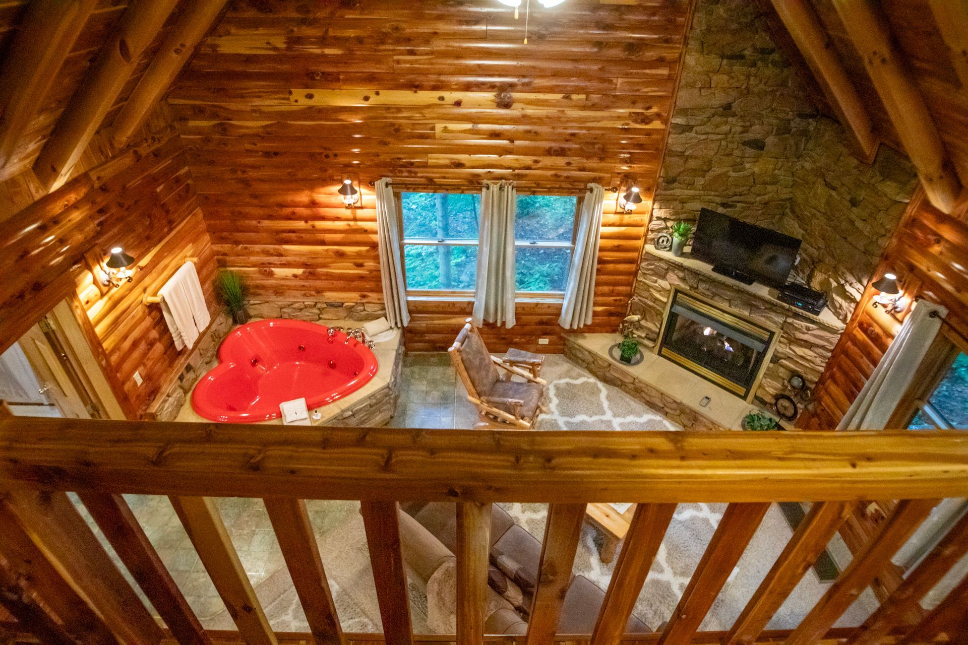 Wooden cabin loft with a red heart-shaped jacuzzi, fireplace, and a rocking chair.