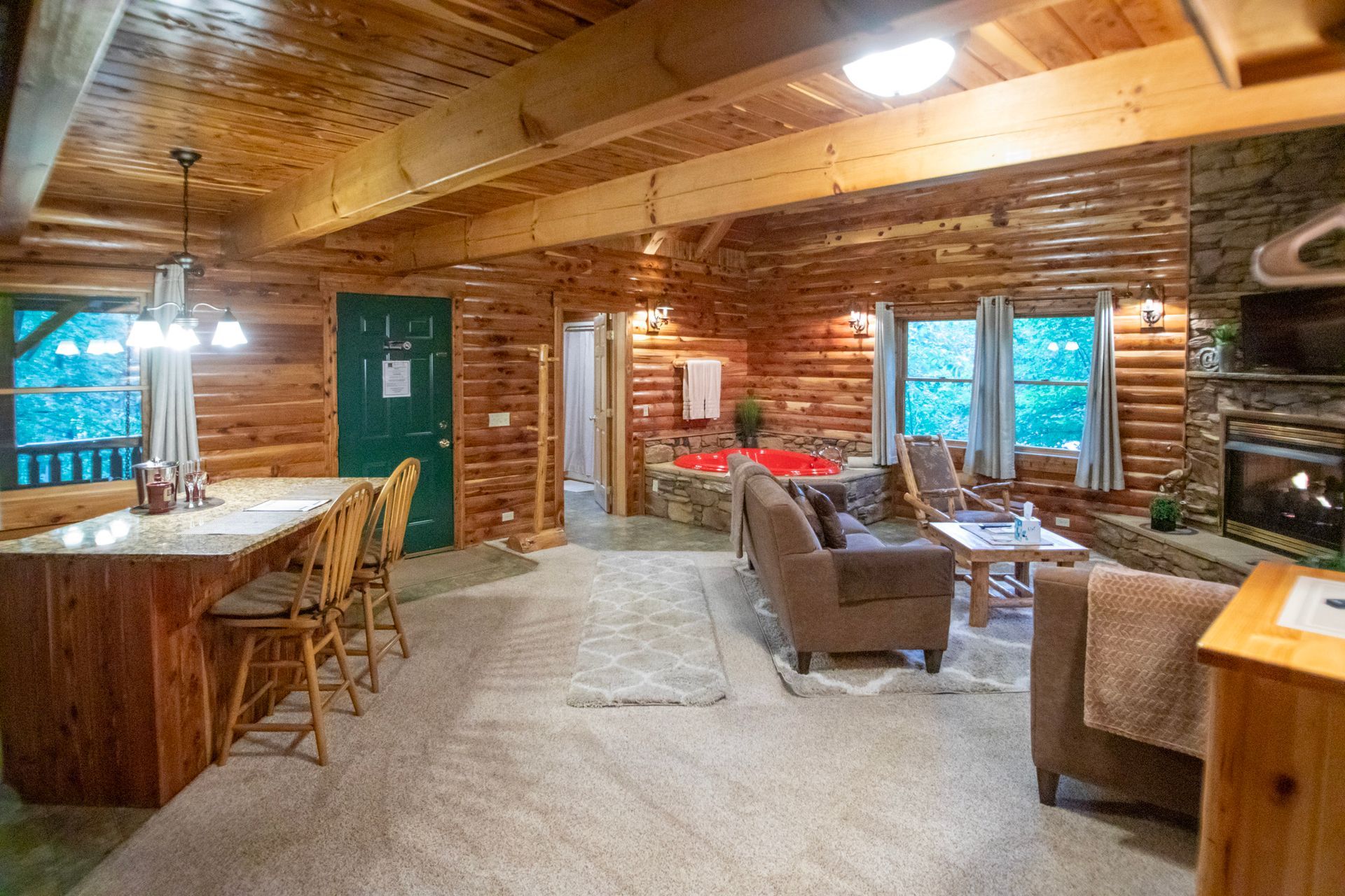 Cozy log cabin interior with kitchen, living area, and fireplace. Wooden beams, neutral tones, and window views.