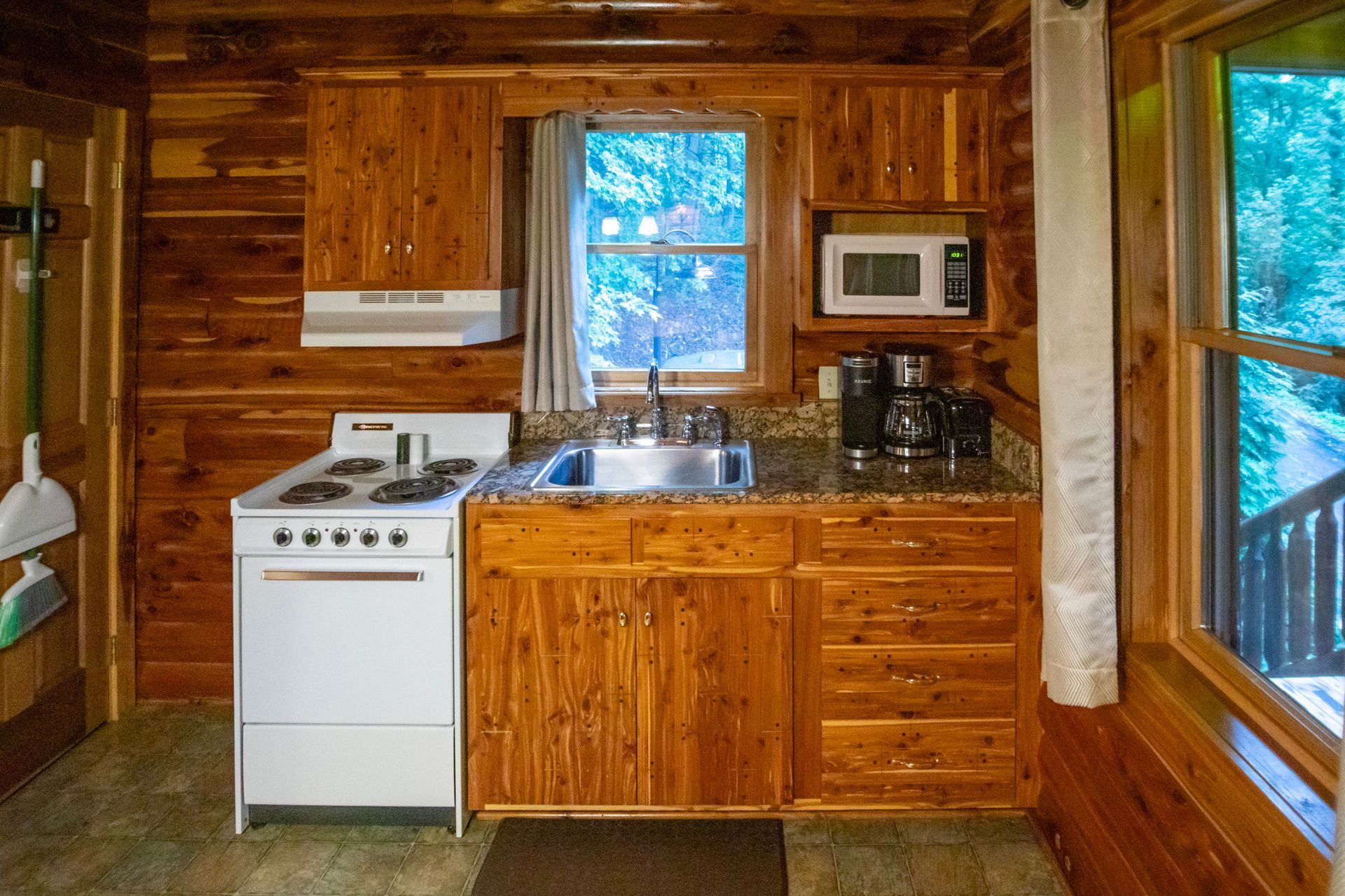 Small cabin kitchen with white stove, microwave, and sink, surrounded by wood paneling.