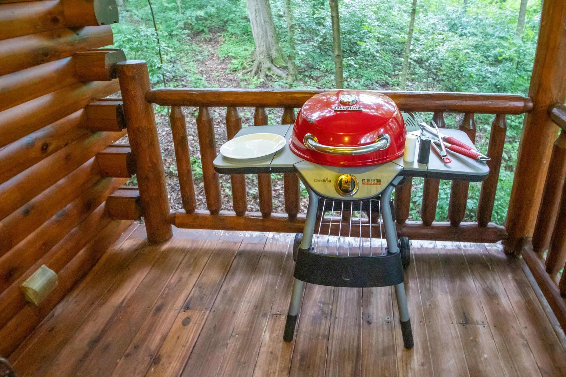 Red charcoal grill on a wooden deck with a forest backdrop.
