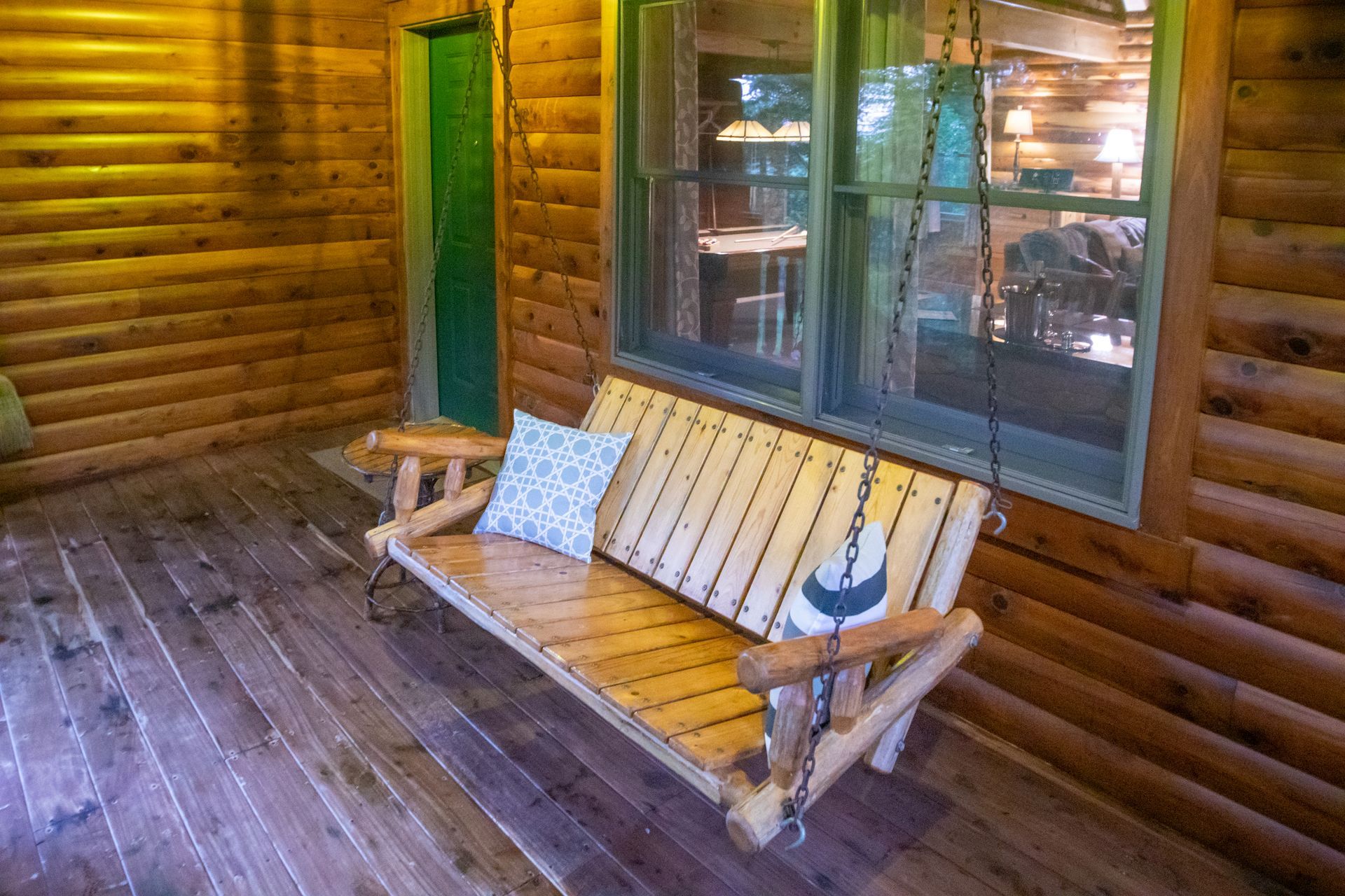 Wooden porch swing with a blue pillow, next to a window.