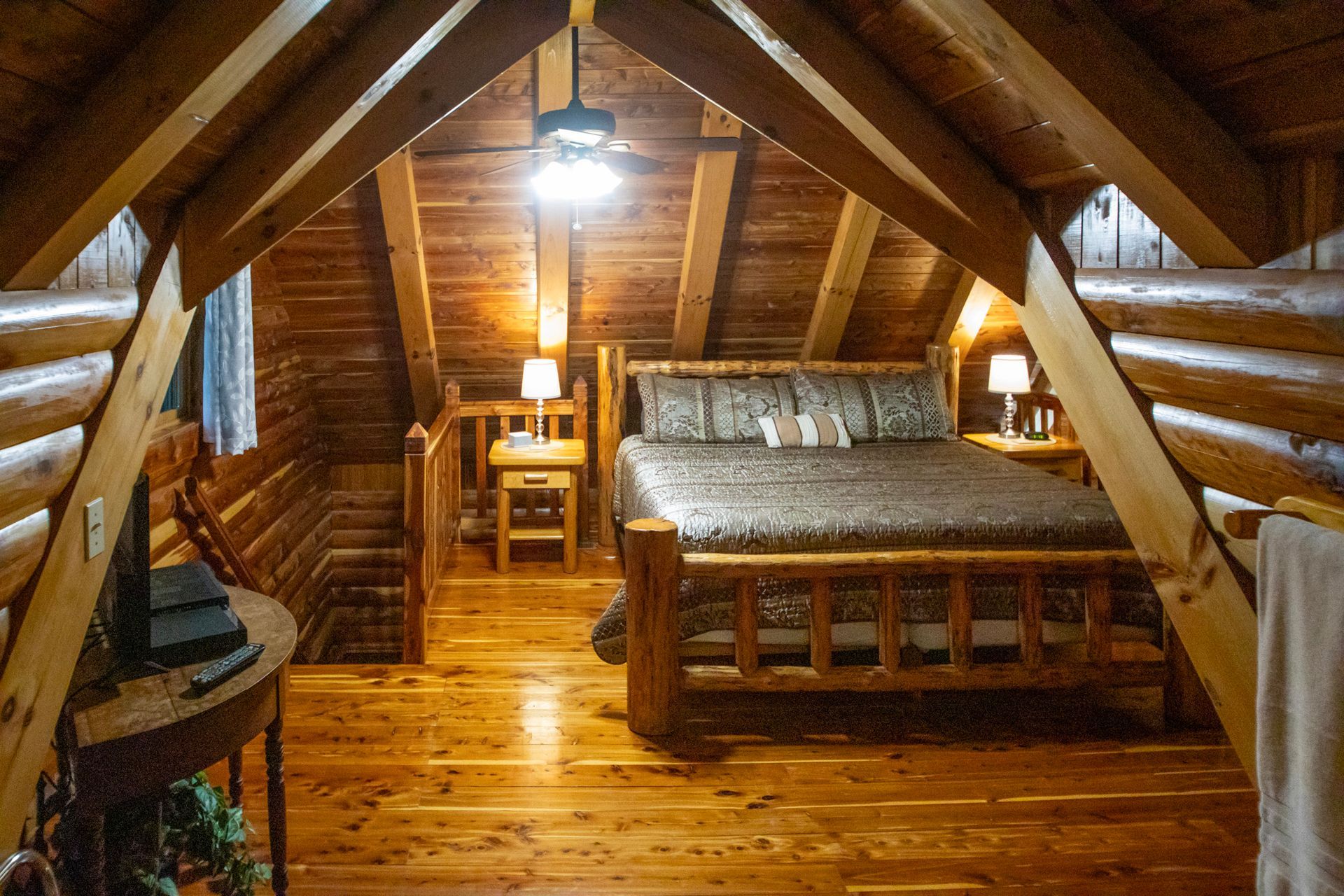 Cozy cabin bedroom with wooden beams, a bed, nightstands, and a staircase.