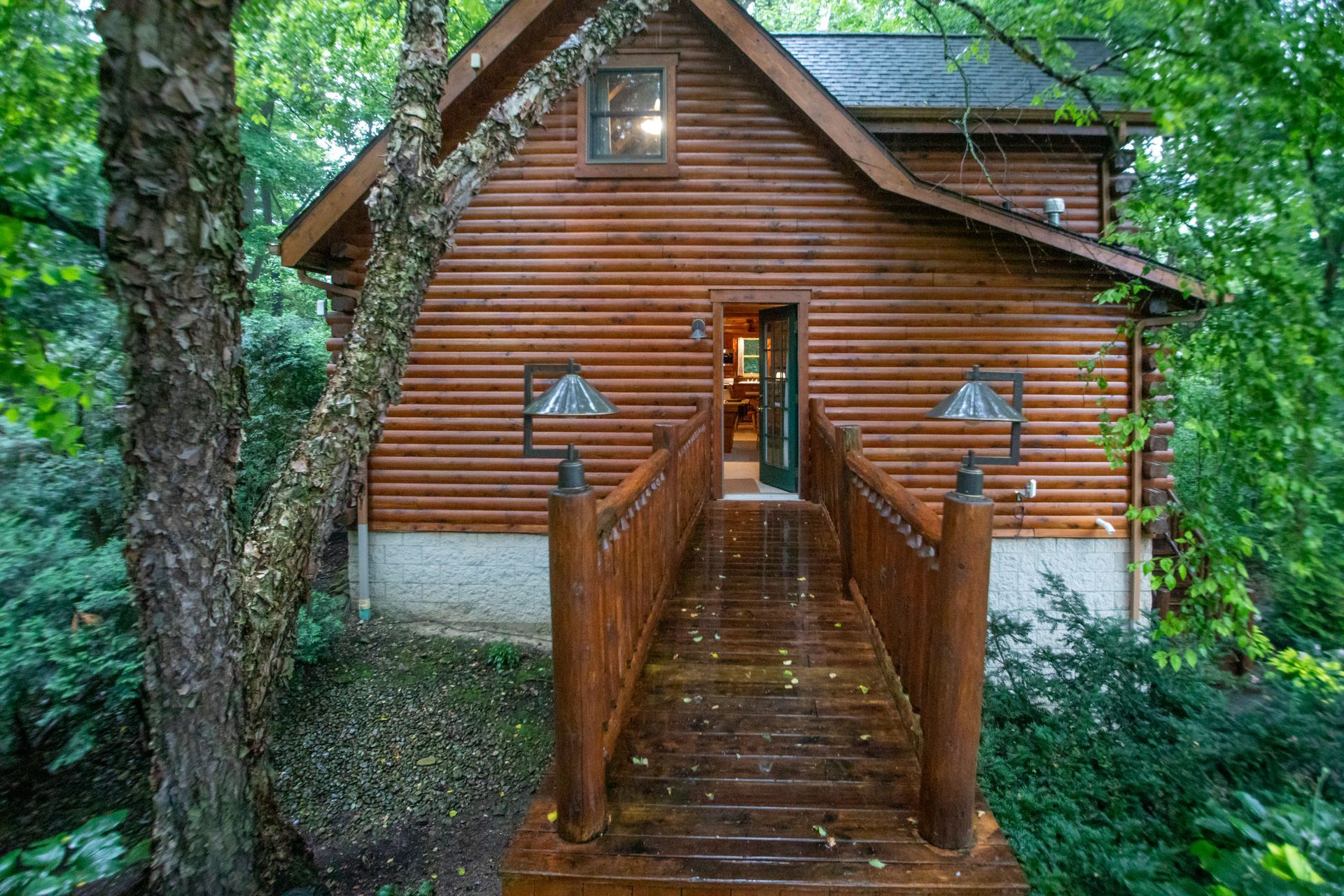 Wooden cabin with bridge entrance surrounded by trees.