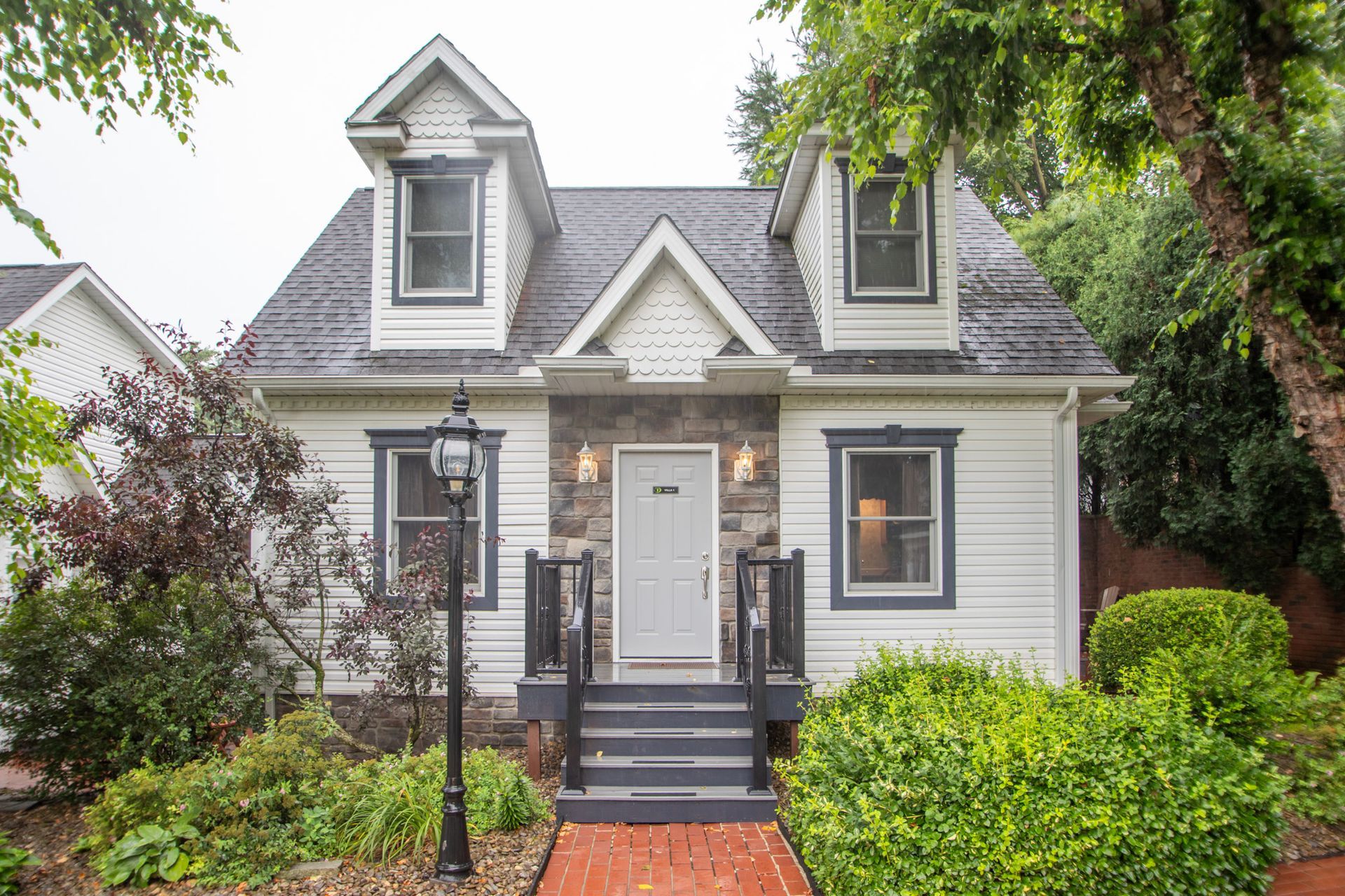 White cottage with gray roof, stone facade, black railings, and landscaping.
