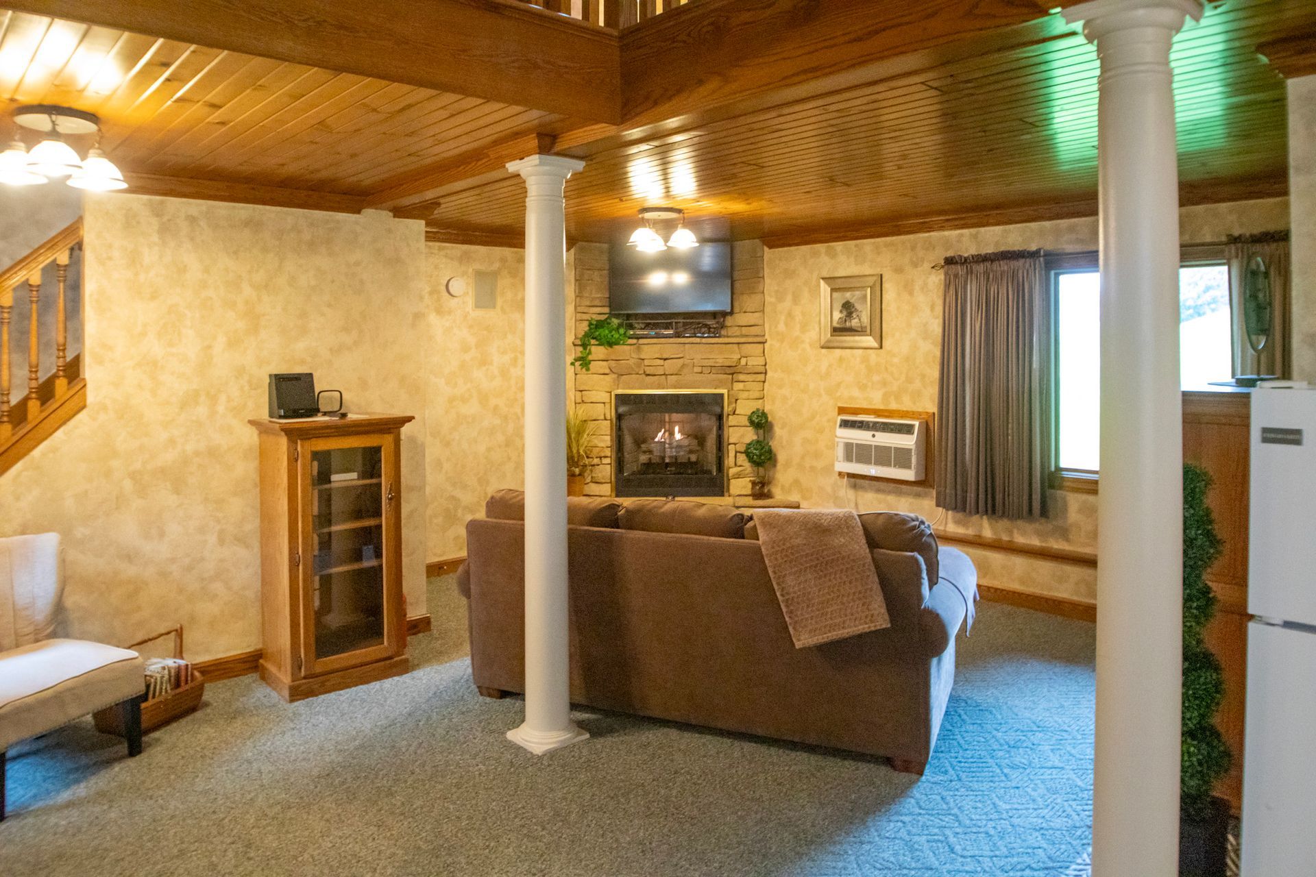 Cozy living room with fireplace, brown sofa, pillars, and wood ceiling.