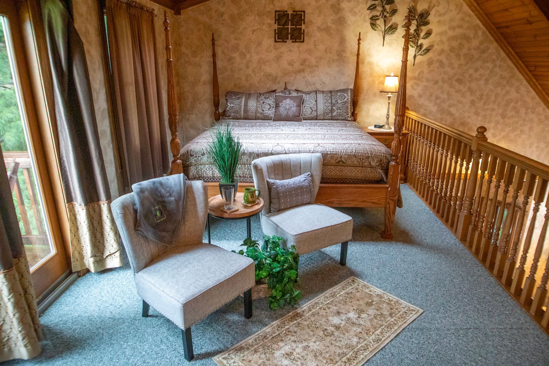 Cozy bedroom loft with a bed, two chairs, and a small table; wooden railing and curtains.