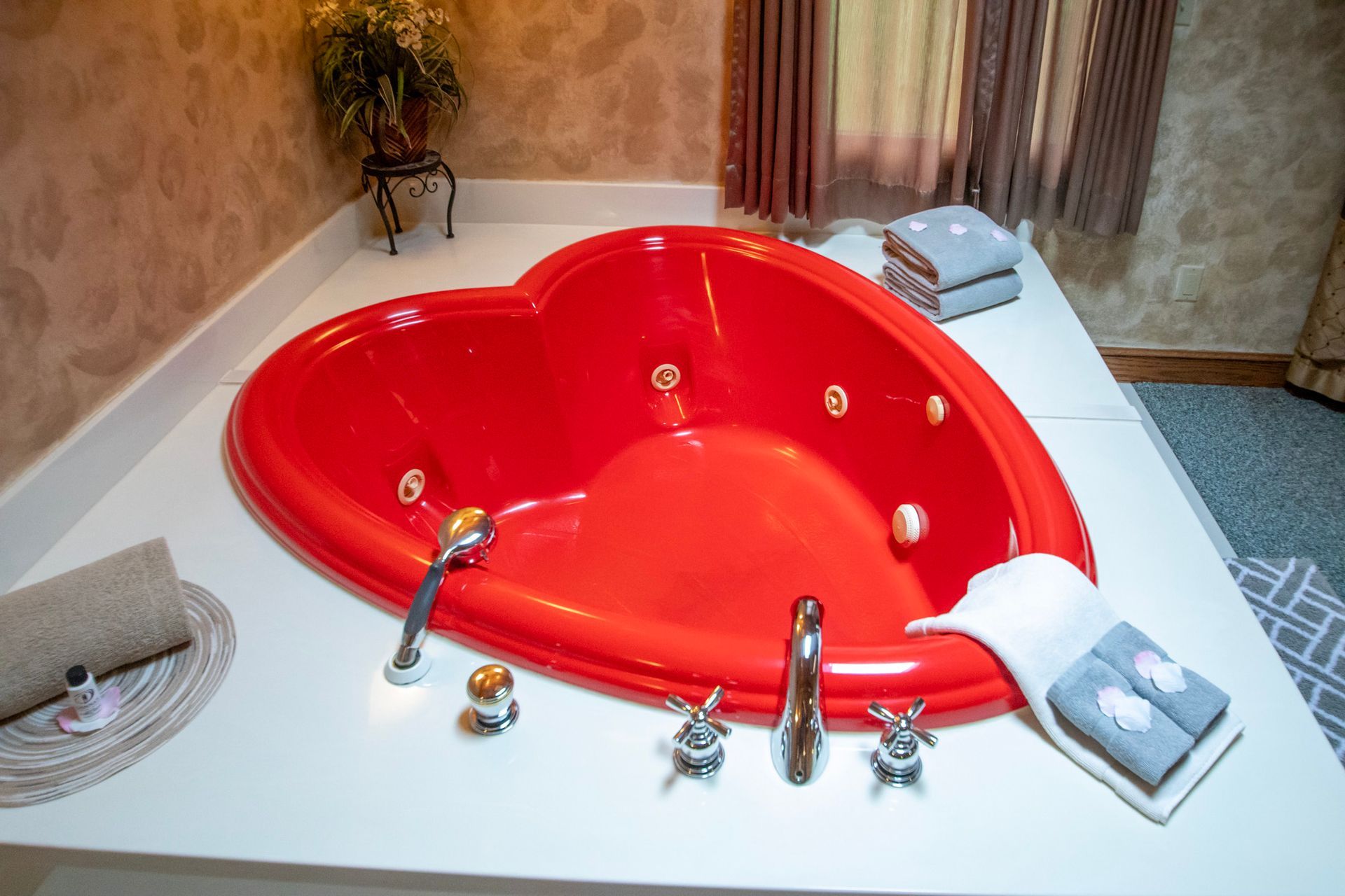 Red heart-shaped jacuzzi tub on a white platform, with towels and fixtures in a bathroom setting.