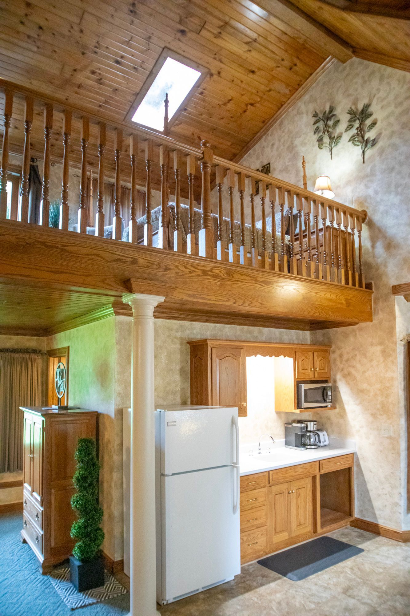 Interior with a wooden loft, kitchen, and skylight. Light-colored cabinets, white fridge, and textured walls.