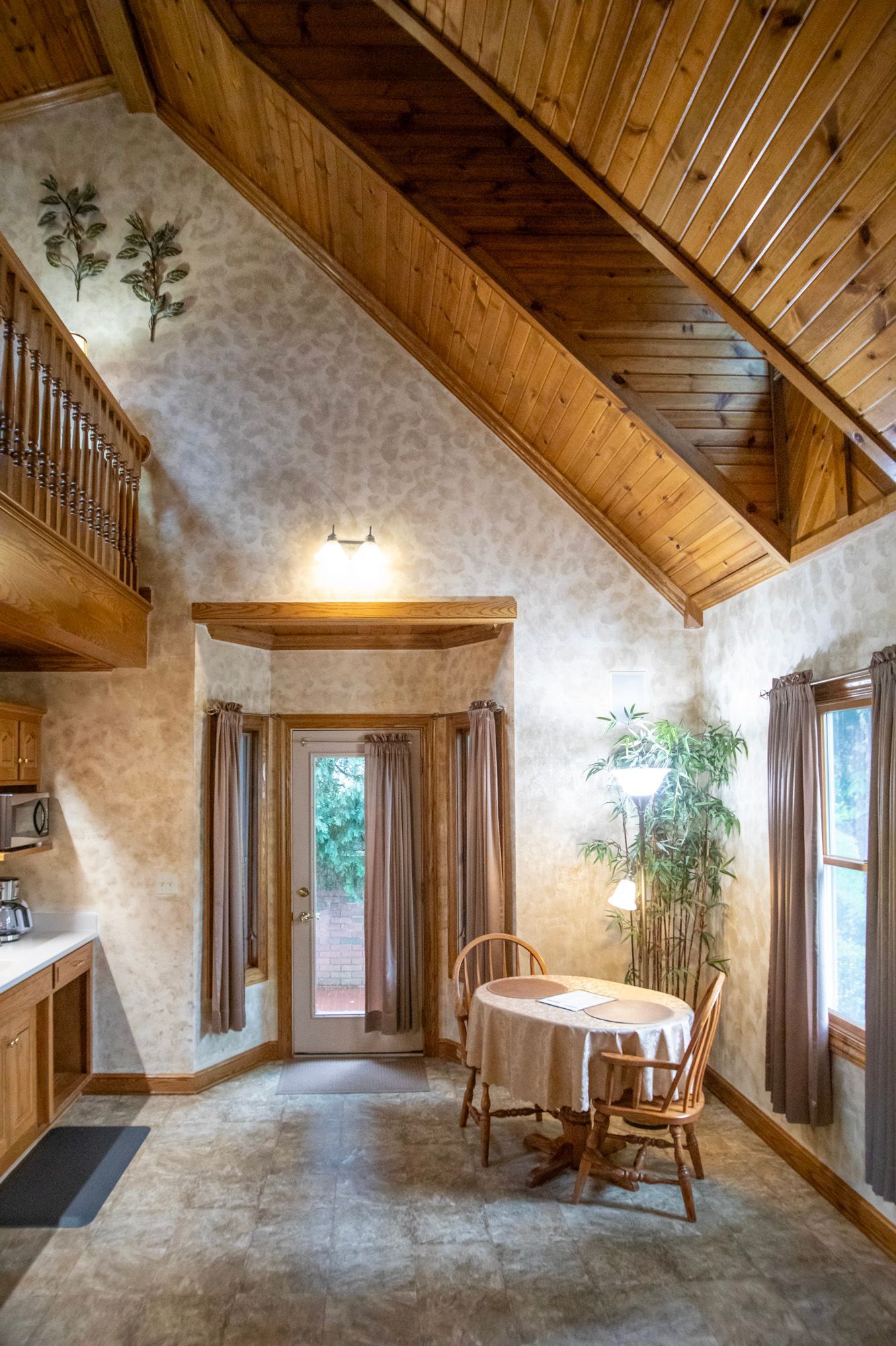 Interior of a room with a loft, wooden beams, a dining table, and a door to the outside.