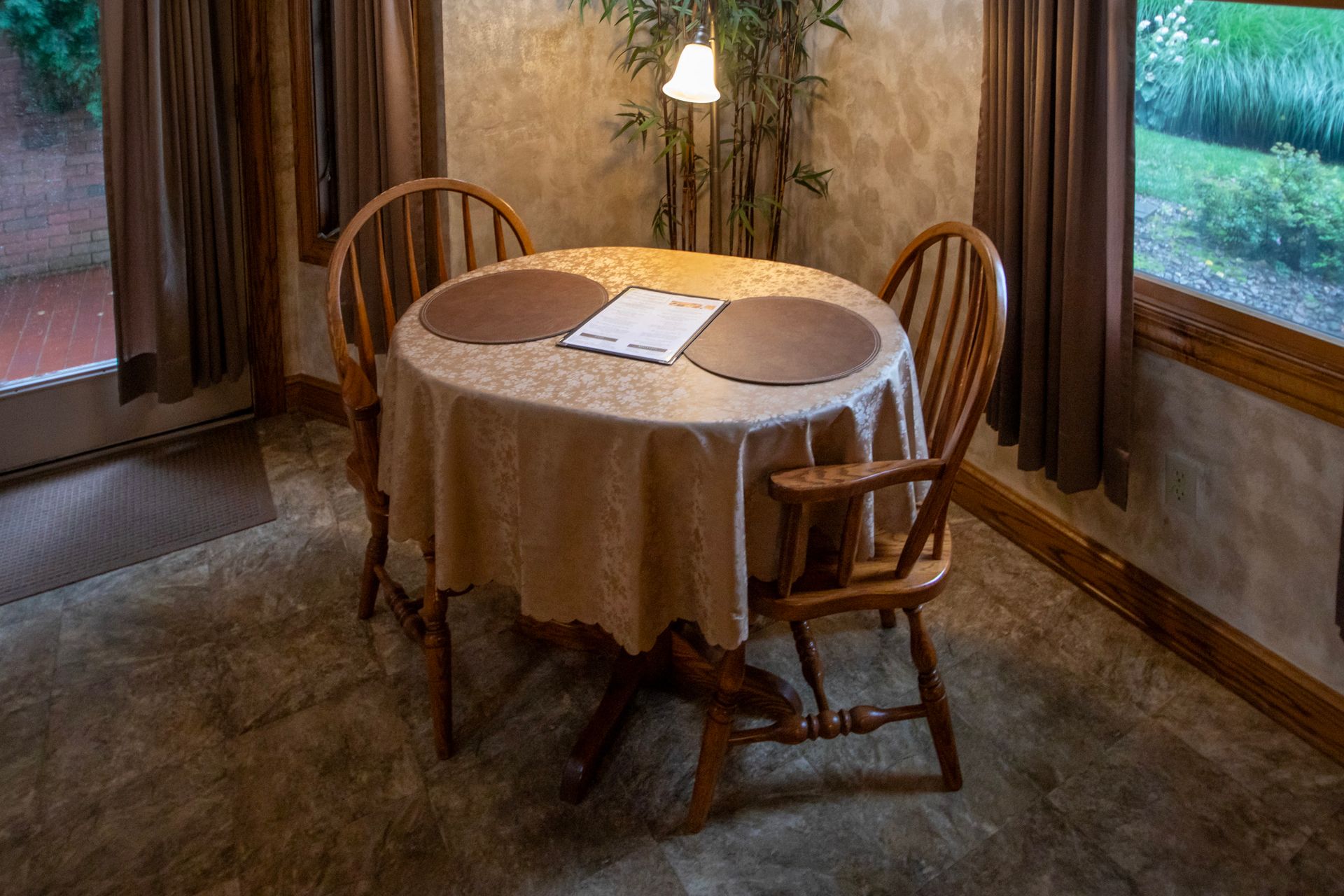 Round table set for two with wooden chairs and a window view.