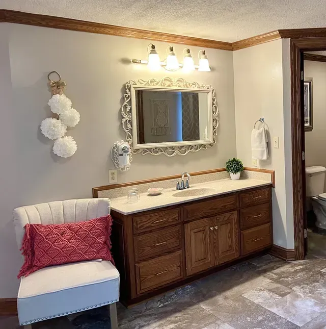 Bathroom with vanity, mirror, chair, and decorative elements. Features wood trim and a pink pillow.