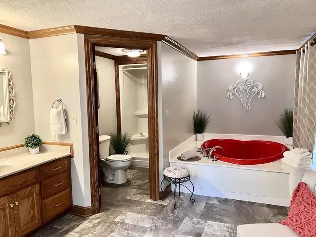 Bathroom with red jacuzzi, toilet, shower, vanity, and stool.