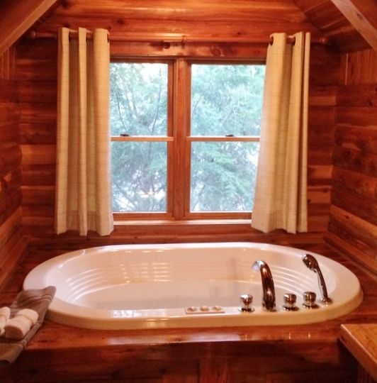 Wooden-walled bathroom with oval tub, window, and cream curtains.