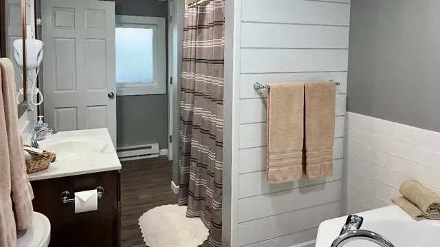 Bathroom interior with wooden floor, white vanity, shiplap wall, and tan towels.