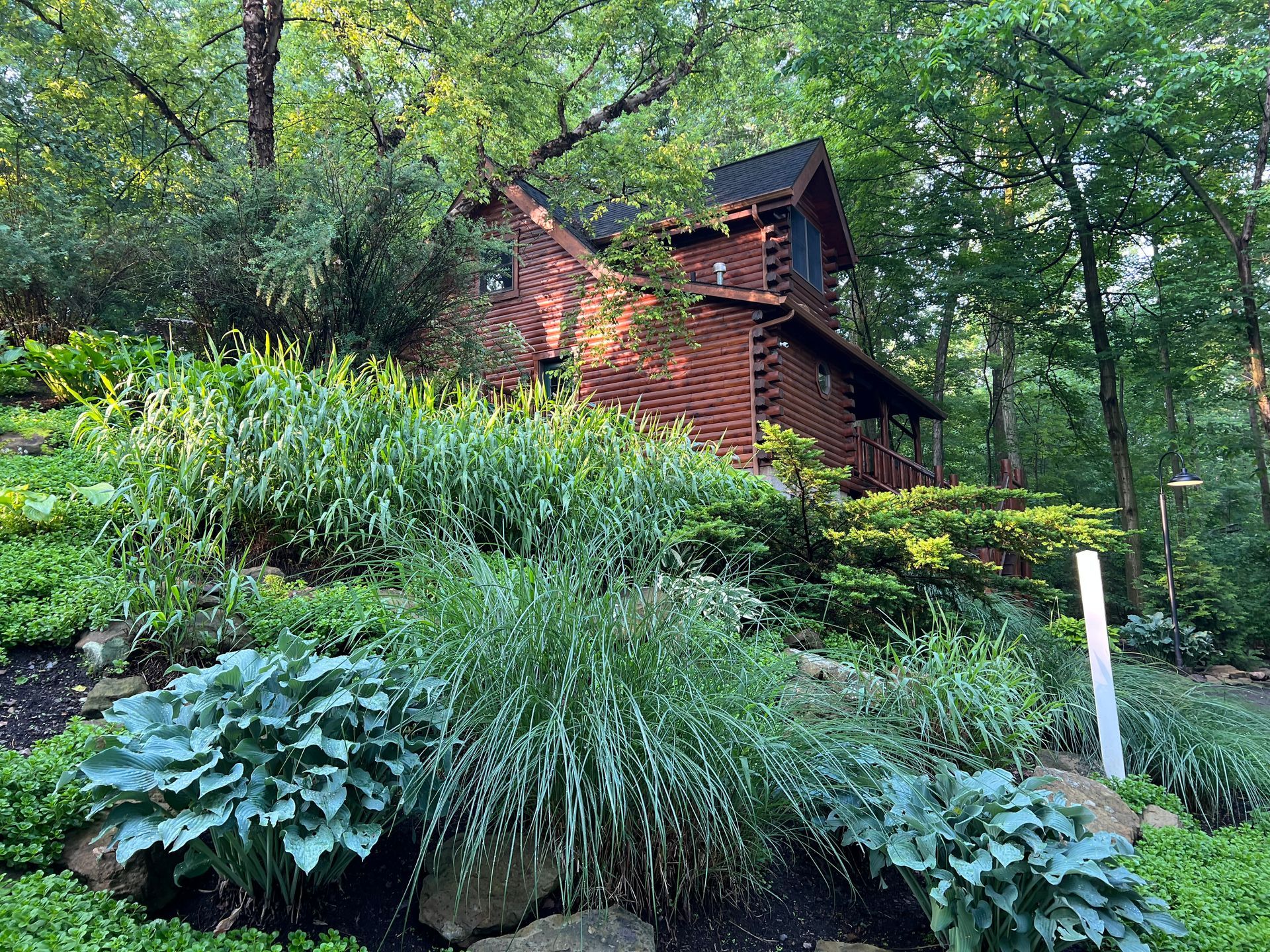 Brown wooden cabin nestled in lush green hillside garden.
