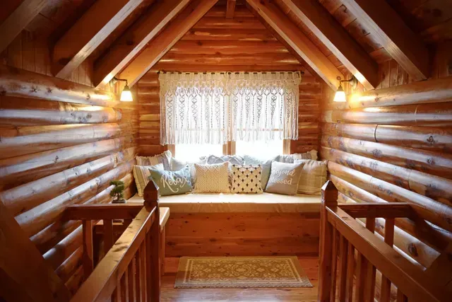 Cozy wooden cabin nook with window seat, pillows, macrame curtain, and small rug.