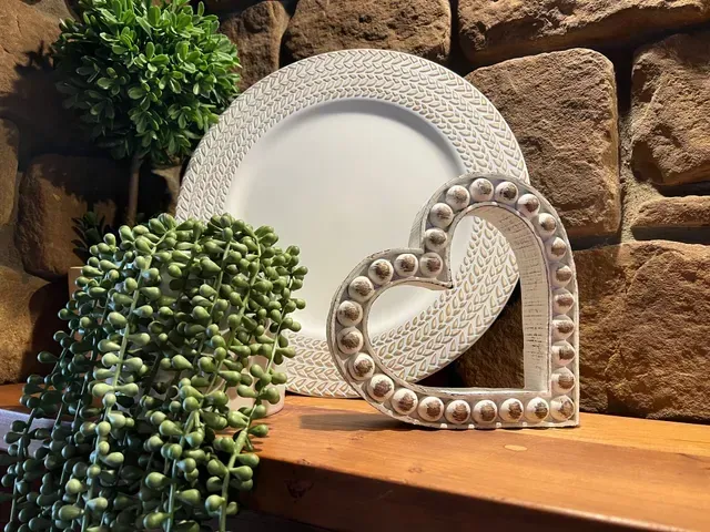 White plate and heart-shaped decoration with faux greenery on a wooden surface against a stone wall.