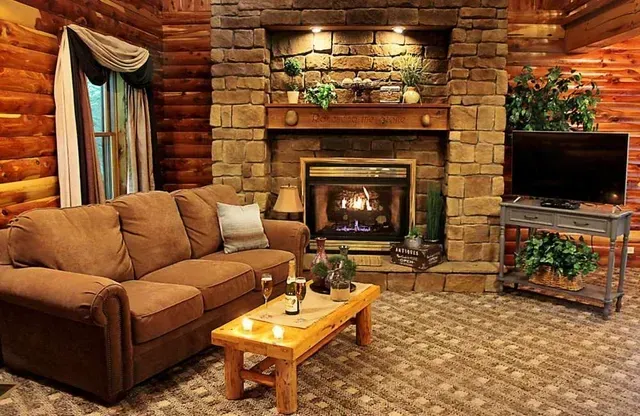 Cozy cabin living room with stone fireplace, brown couch, TV, and wooden furniture.