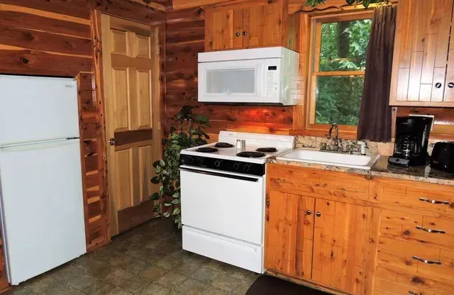Kitchen with white appliances and wooden cabinetry in a log cabin.