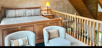 Bedroom with wooden bed, two armchairs, and loft railing.