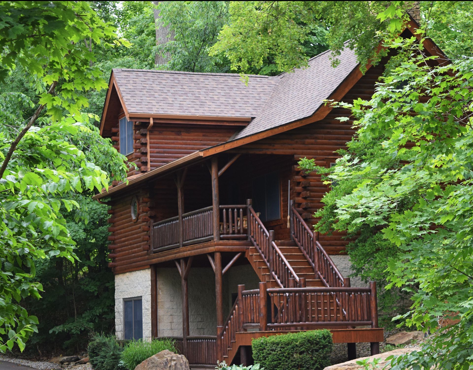Wooden cabin nestled in greenery with an exterior staircase and balcony.