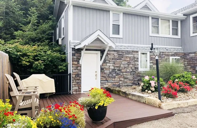 Two-story house with stone facade, white door, and deck with flowers.
