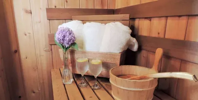 Wooden sauna interior with towels, flowers, drinks, and a wooden bucket with a ladle.