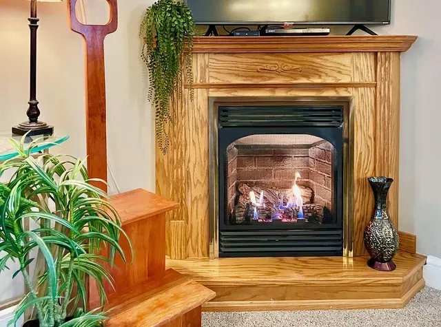 Fireplace with burning flames, wooden mantel, and decorative vase.