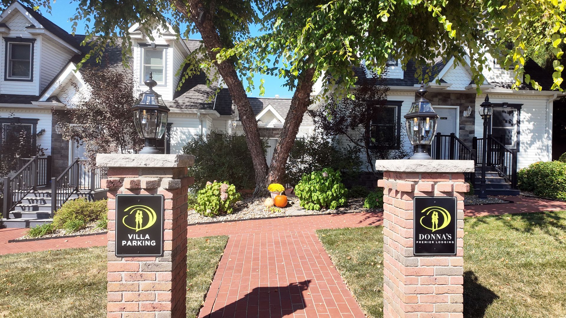 Brick pathway leading to white houses with lamps; fall decor.