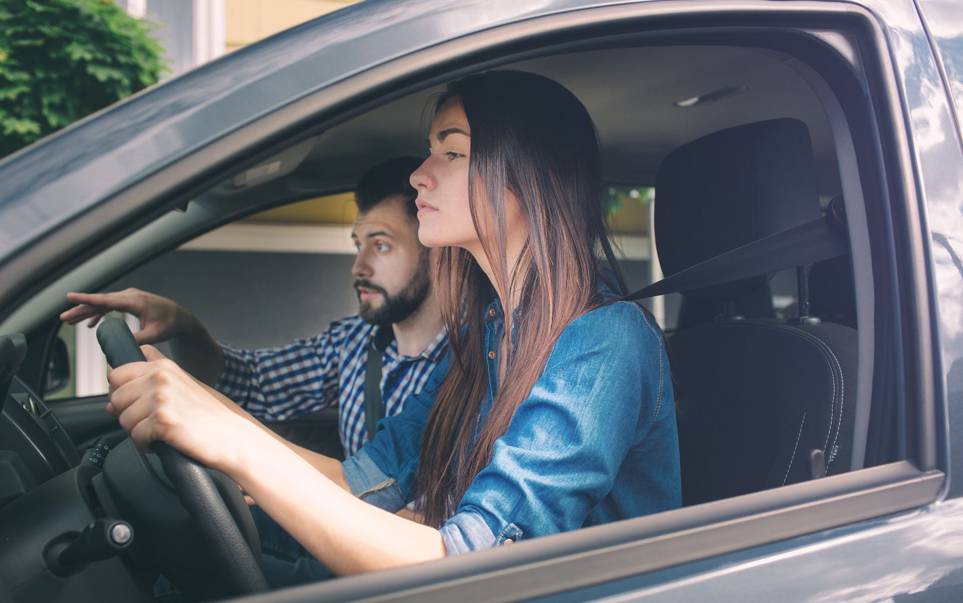 Woman driving a car with a male instructor; she looks focused, he points toward the road. Woman driving a car with a male instructor; she looks focused, he points toward the road.