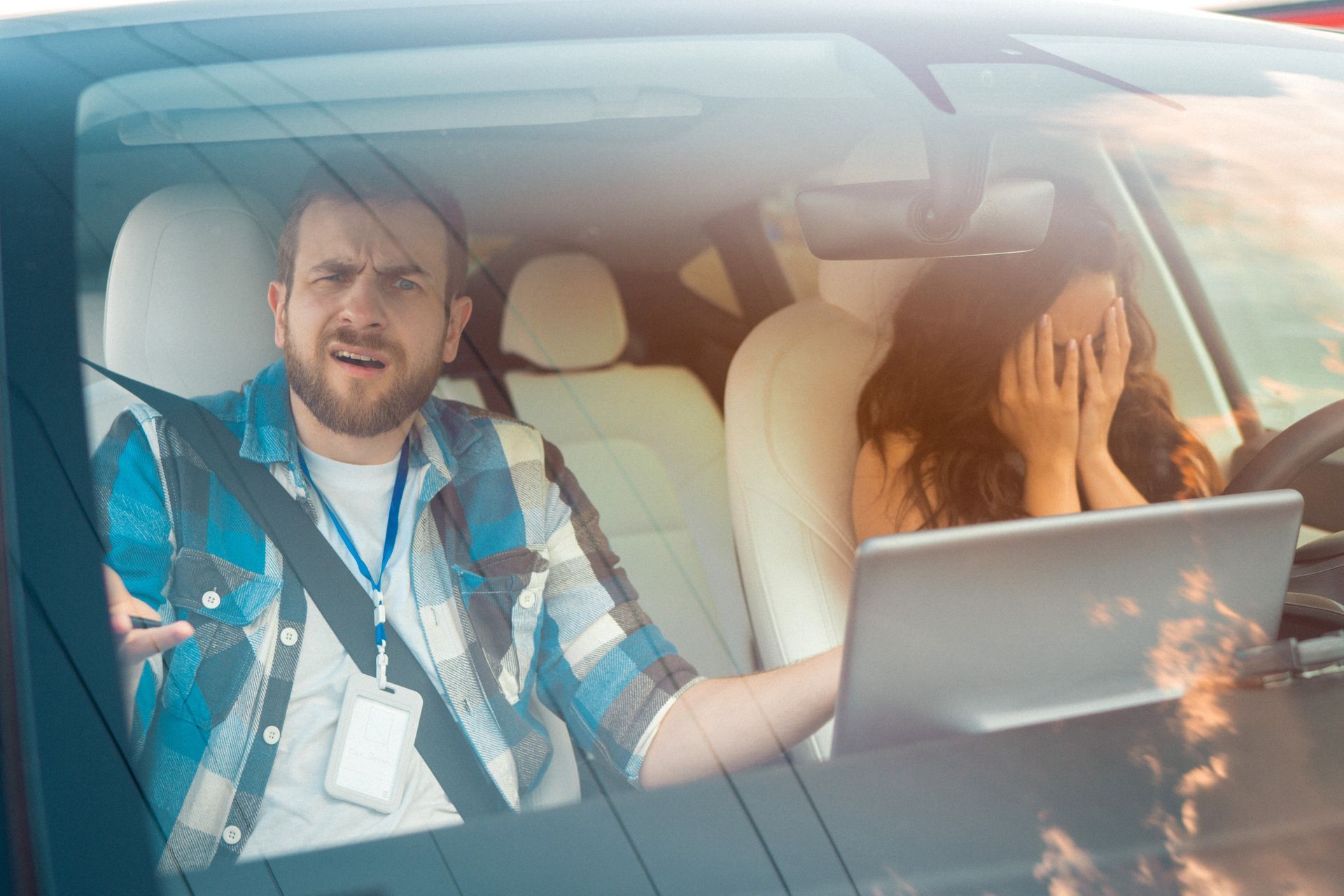 Man in plaid shirt gestures angrily at woman covering face, laptop on steering wheel, in car. Man in plaid shirt gestures angrily at woman covering face, laptop on steering wheel, in car.
