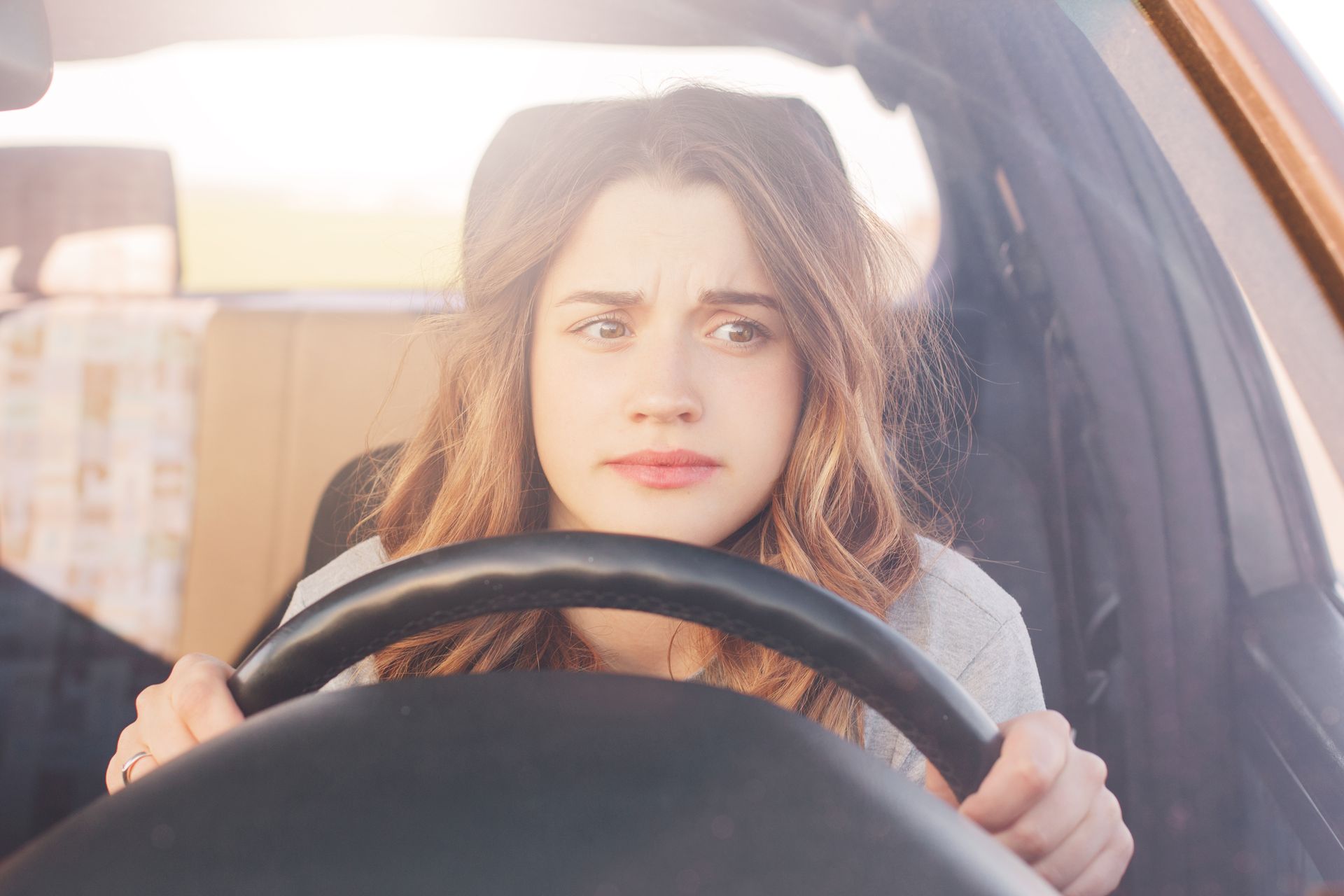 Woman gripping steering wheel with a worried expression, driving a car. Bright sunlight.