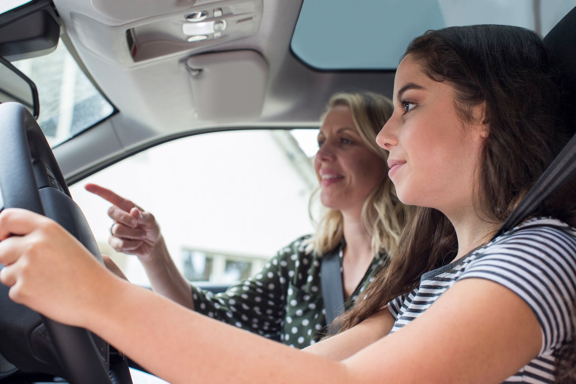 Woman guiding a young driver in a car, pointing ahead, interior view.