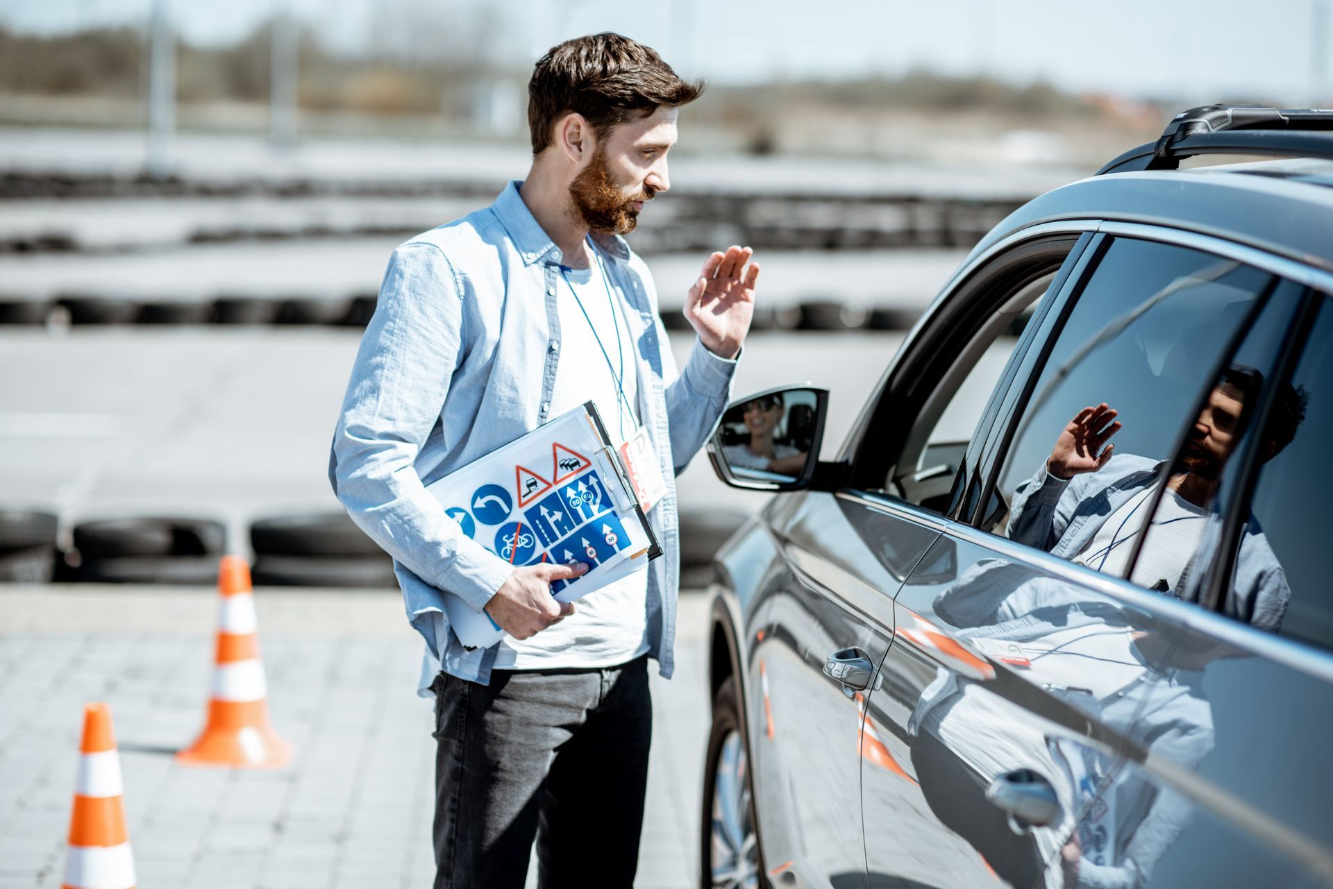 Driving instructor talking to a driver in a car. Outdoor driving course setting.