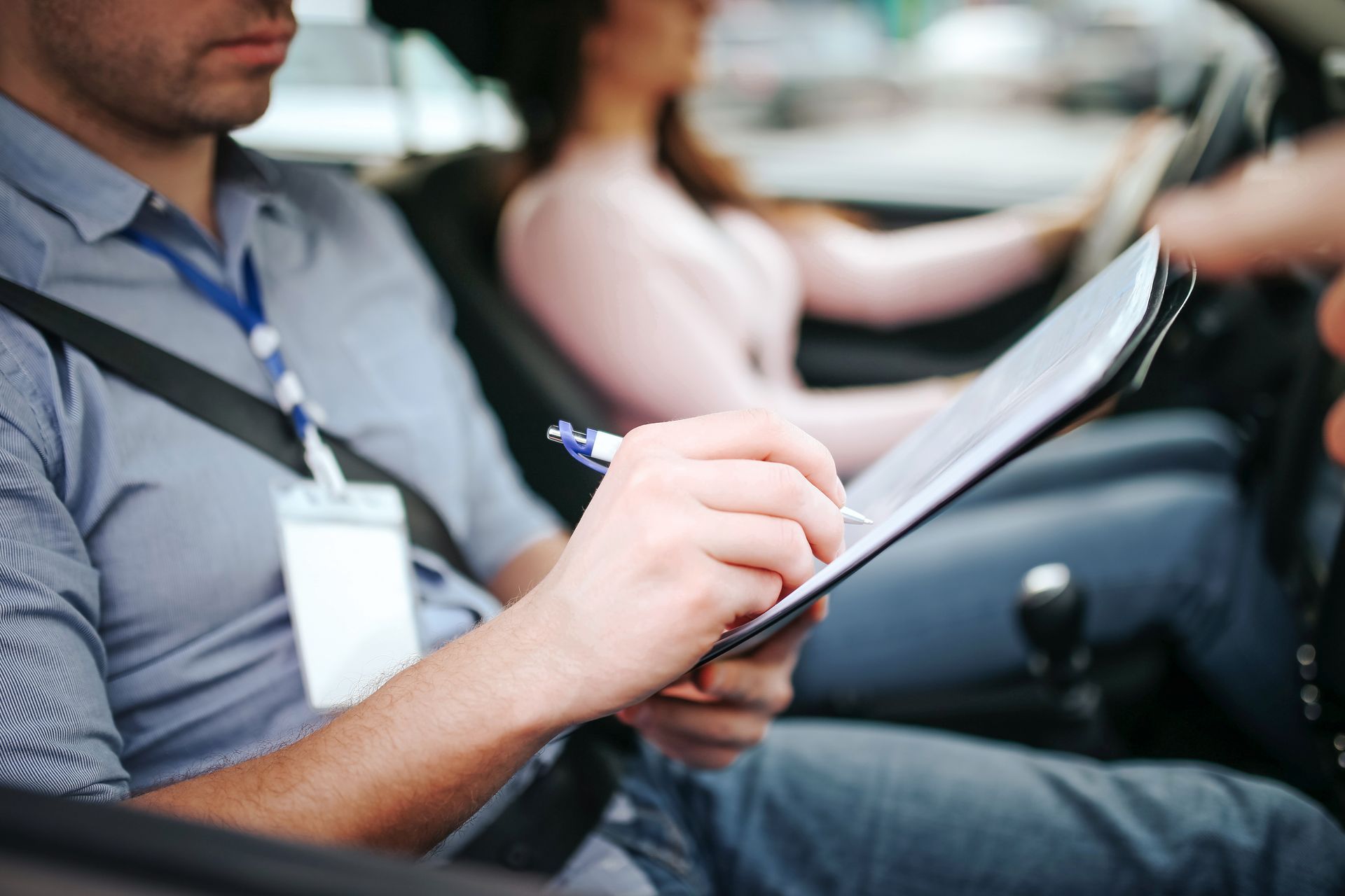 Driving instructor in car, writing on clipboard, student driver at the wheel. Driving instructor in car, writing on clipboard, student driver at the wheel.