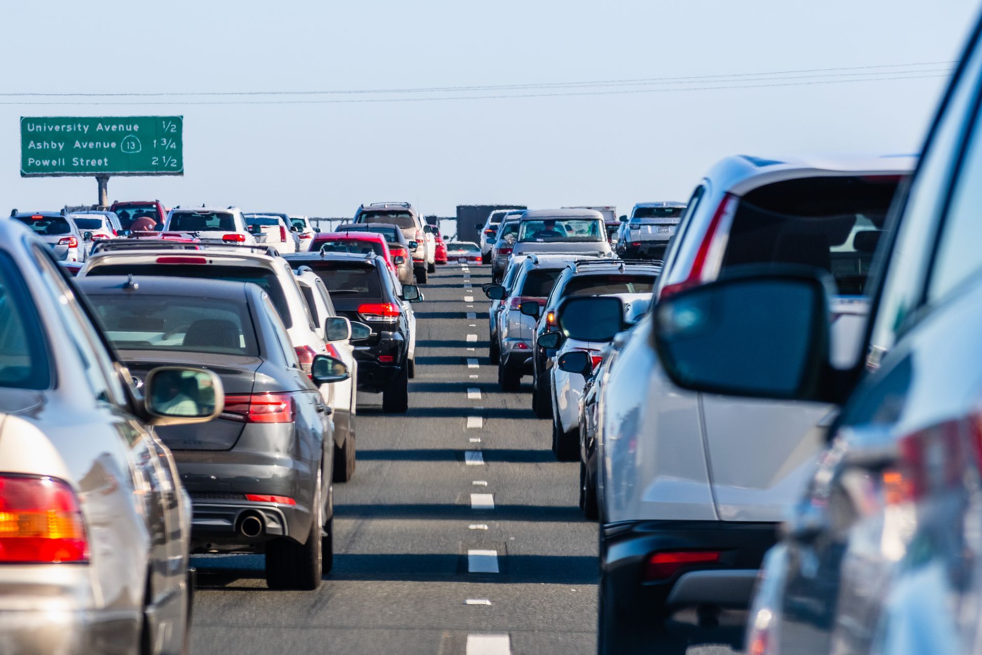 Cars in heavy traffic on a multilane highway, a green sign in the background.