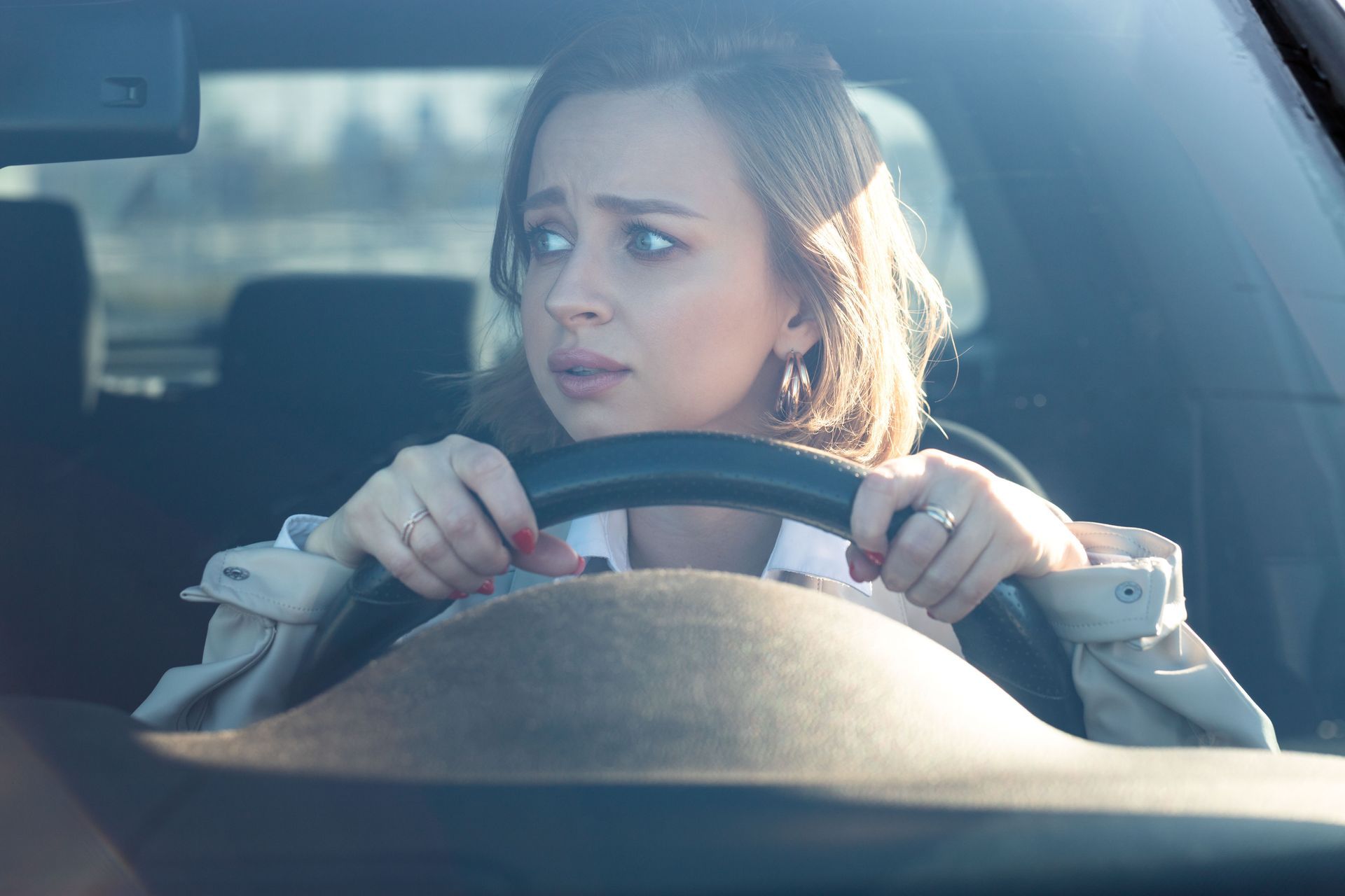 Woman gripping steering wheel, looking fearful while driving.