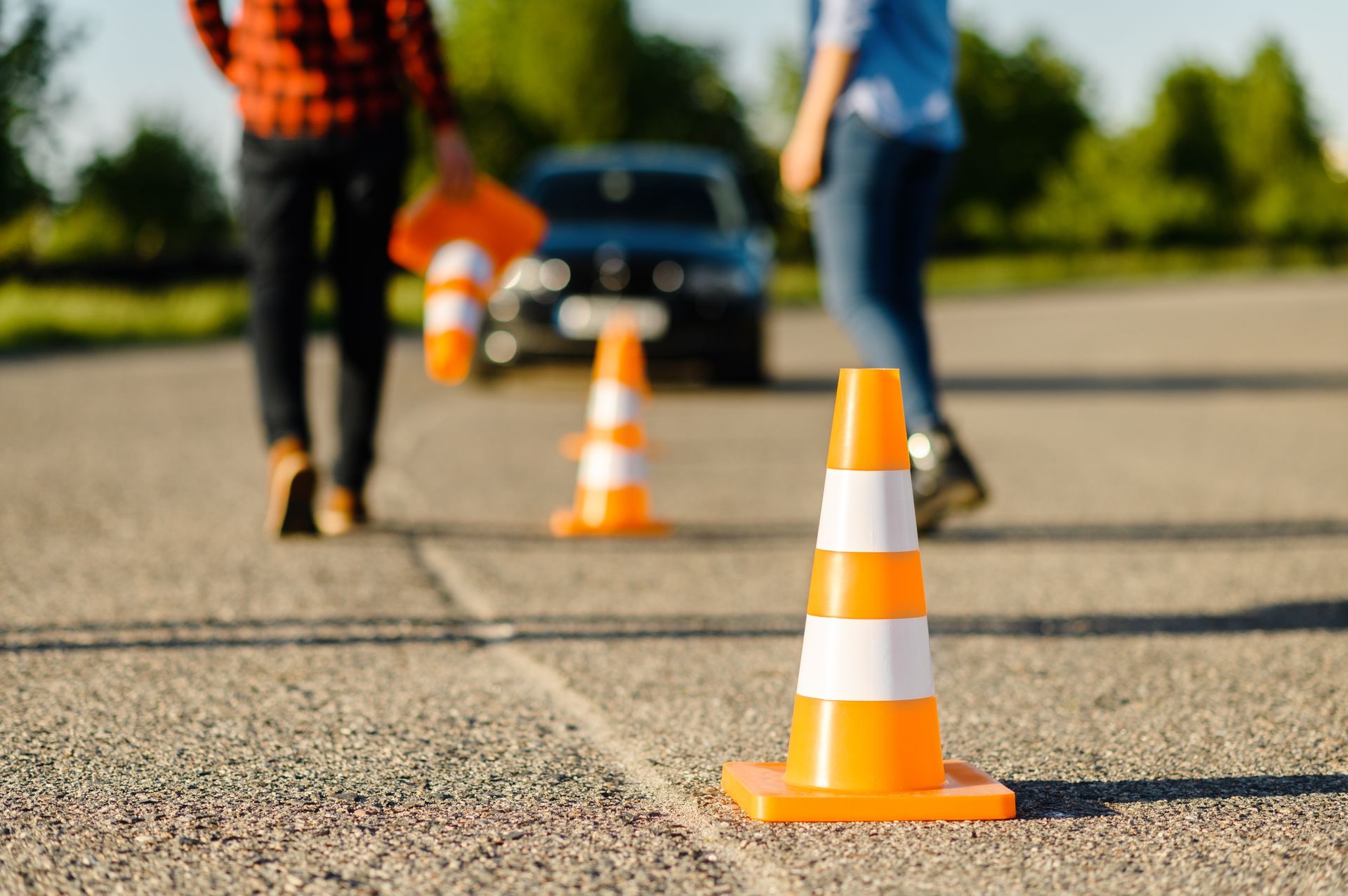 Traffic cones on asphalt with people and a car in the background. Traffic cones on asphalt with people and a car in the background.