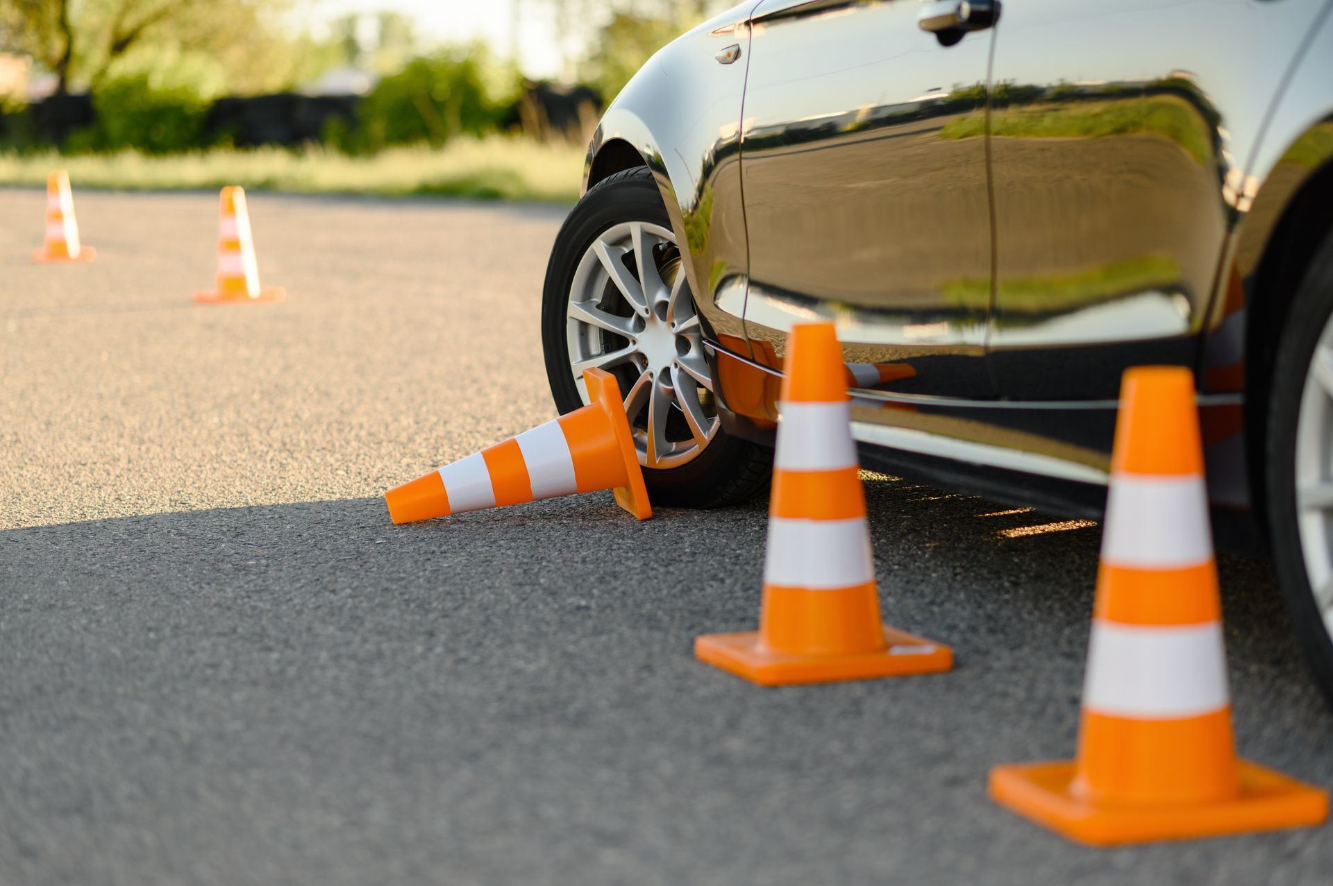 Car driving through orange cones on pavement, knocking one over.