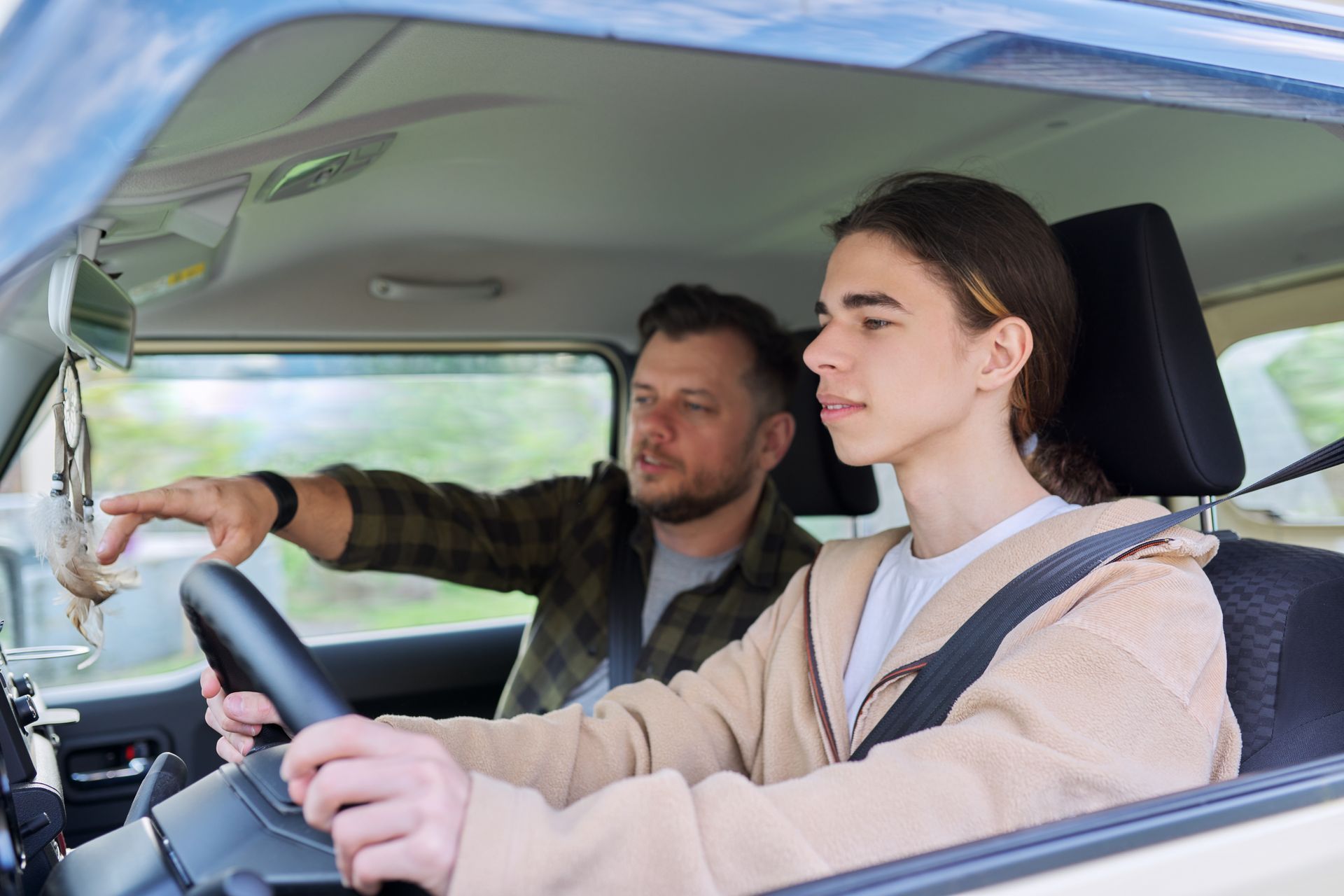 Teen driving a car, instructor points ahead.
