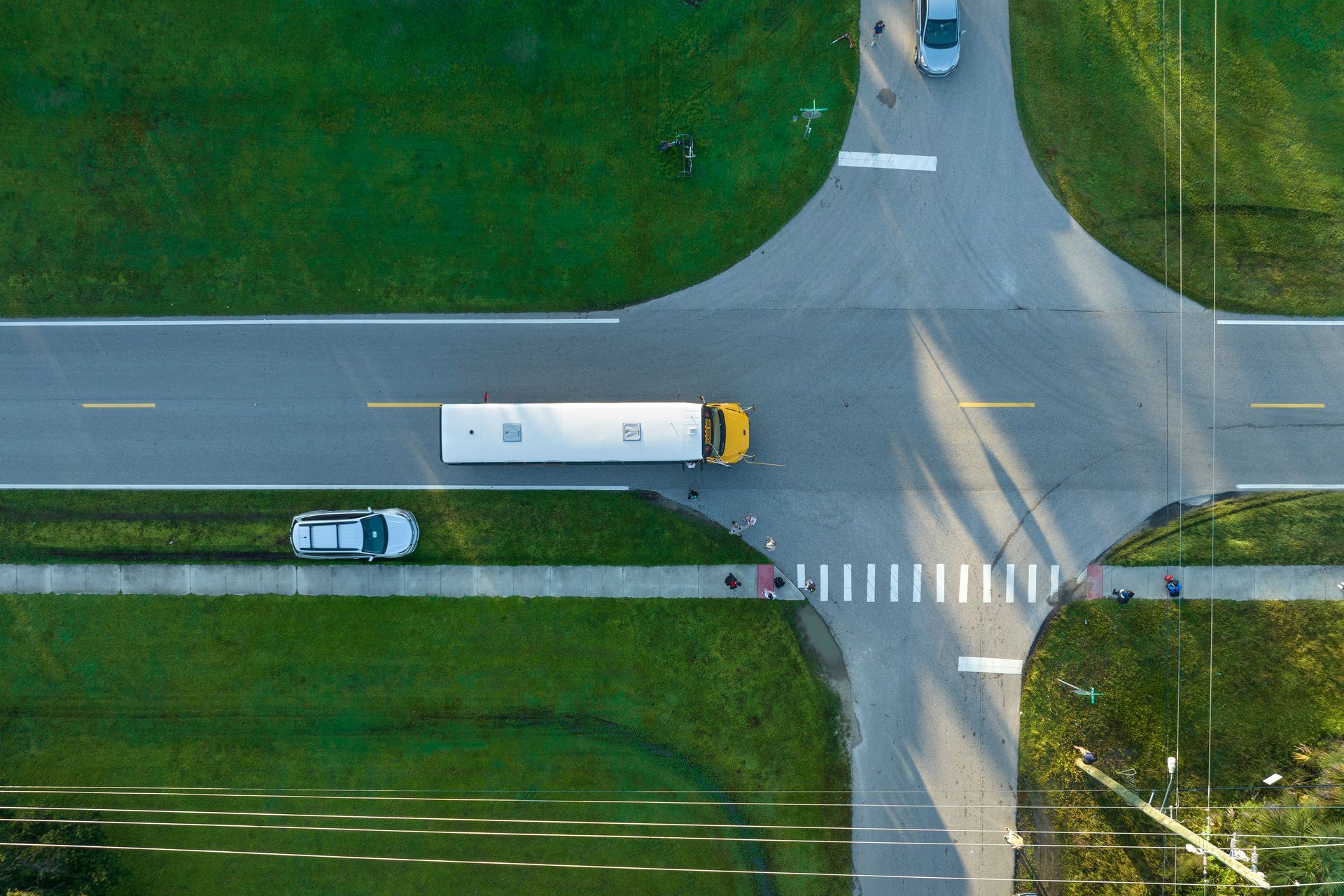 Overhead view of a school bus traveling through a crossroads with a white car in the left lane. Overhead view of a school bus traveling through a crossroads with a white car in the left lane.