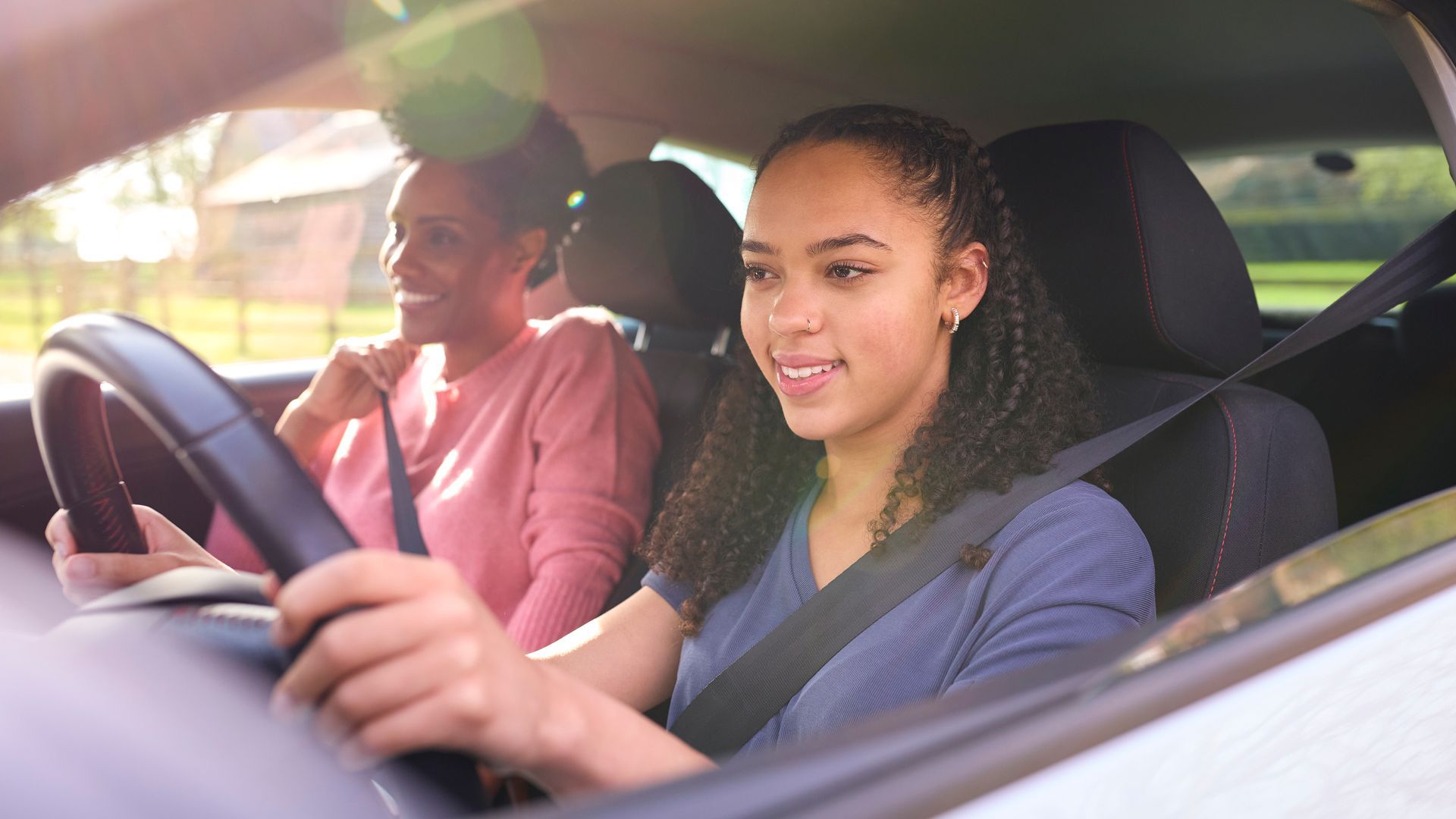 Teenager driving a car with a passenger; both wearing seatbelts. Sunny day. Teenager driving a car with a passenger; both wearing seatbelts. Sunny day.