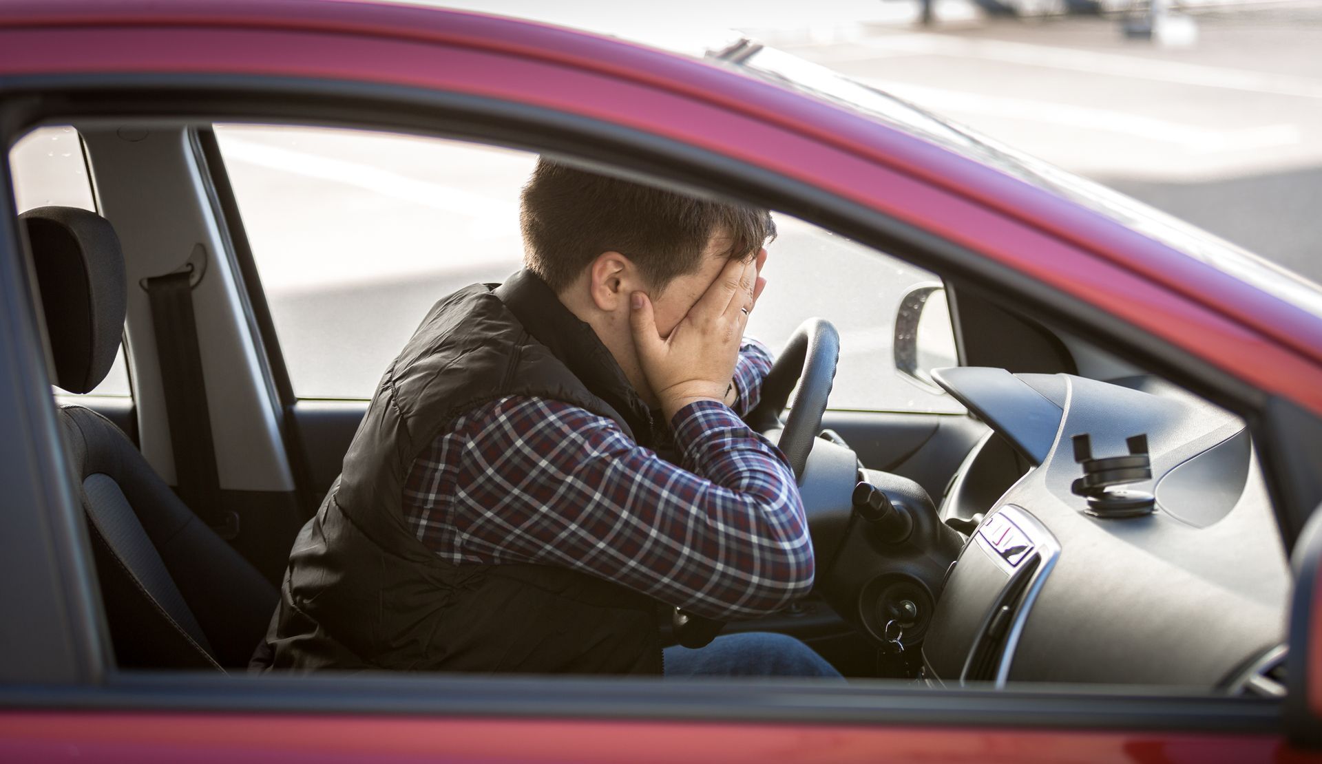 Man in a red car, covering his face with hands, looking stressed. Man in a red car, covering his face with hands, looking stressed.