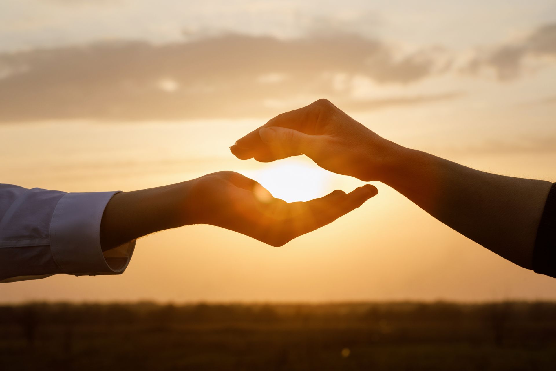 Two people are holding the sun in their hands at sunset.