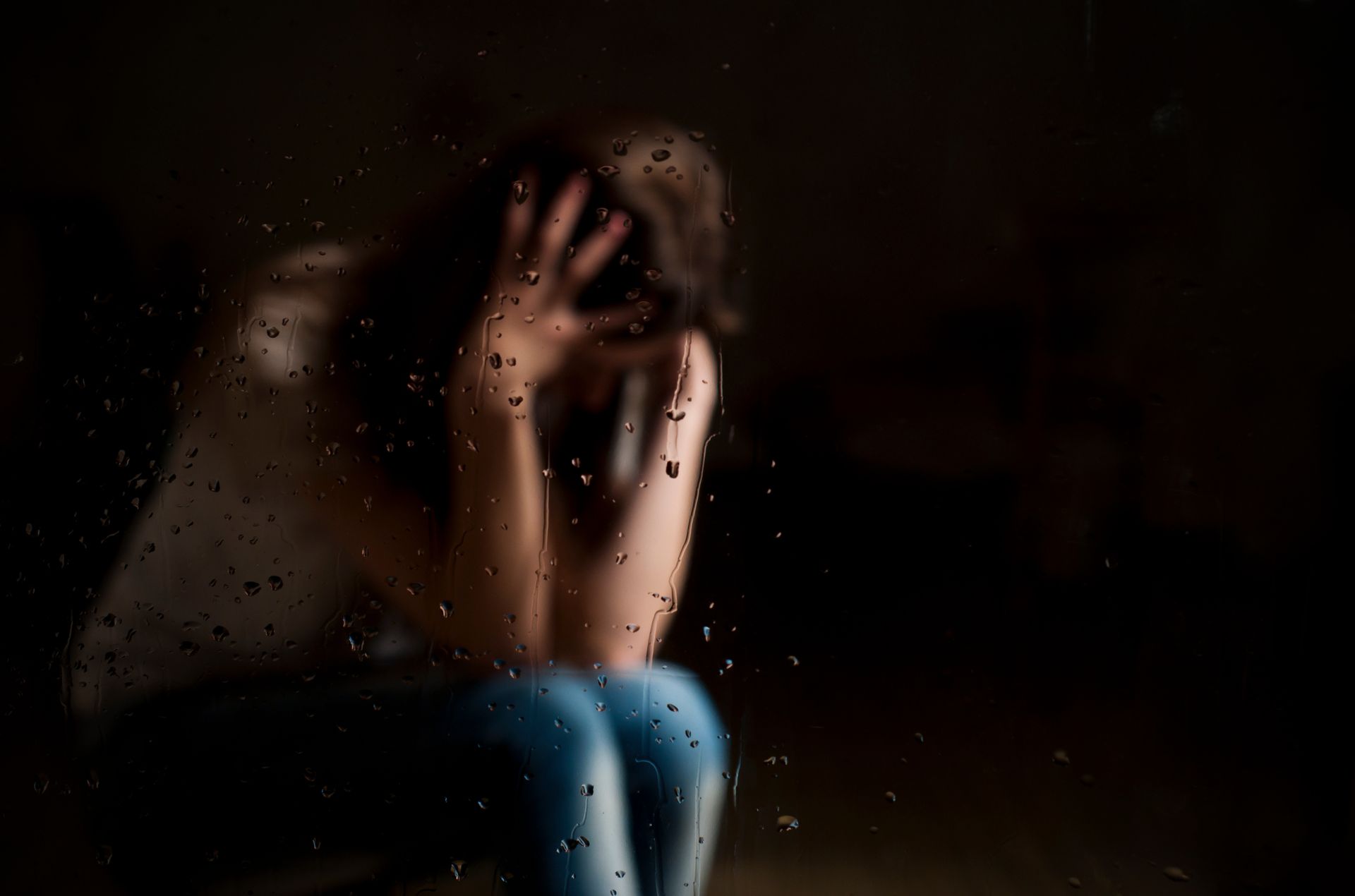A woman is sitting in front of a window with her head in her hands.
