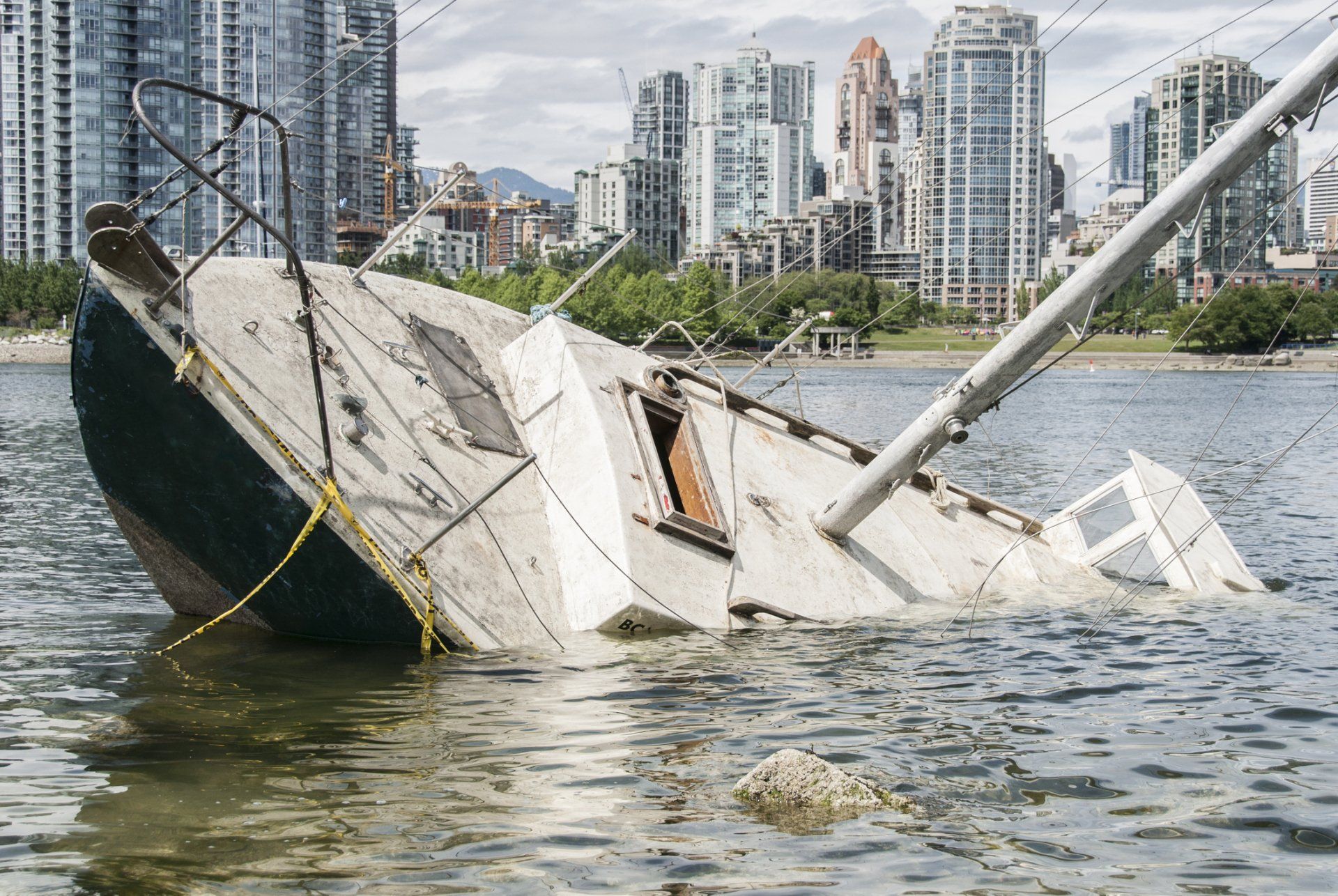 Partially submerged sailboat in water, near city skyline.