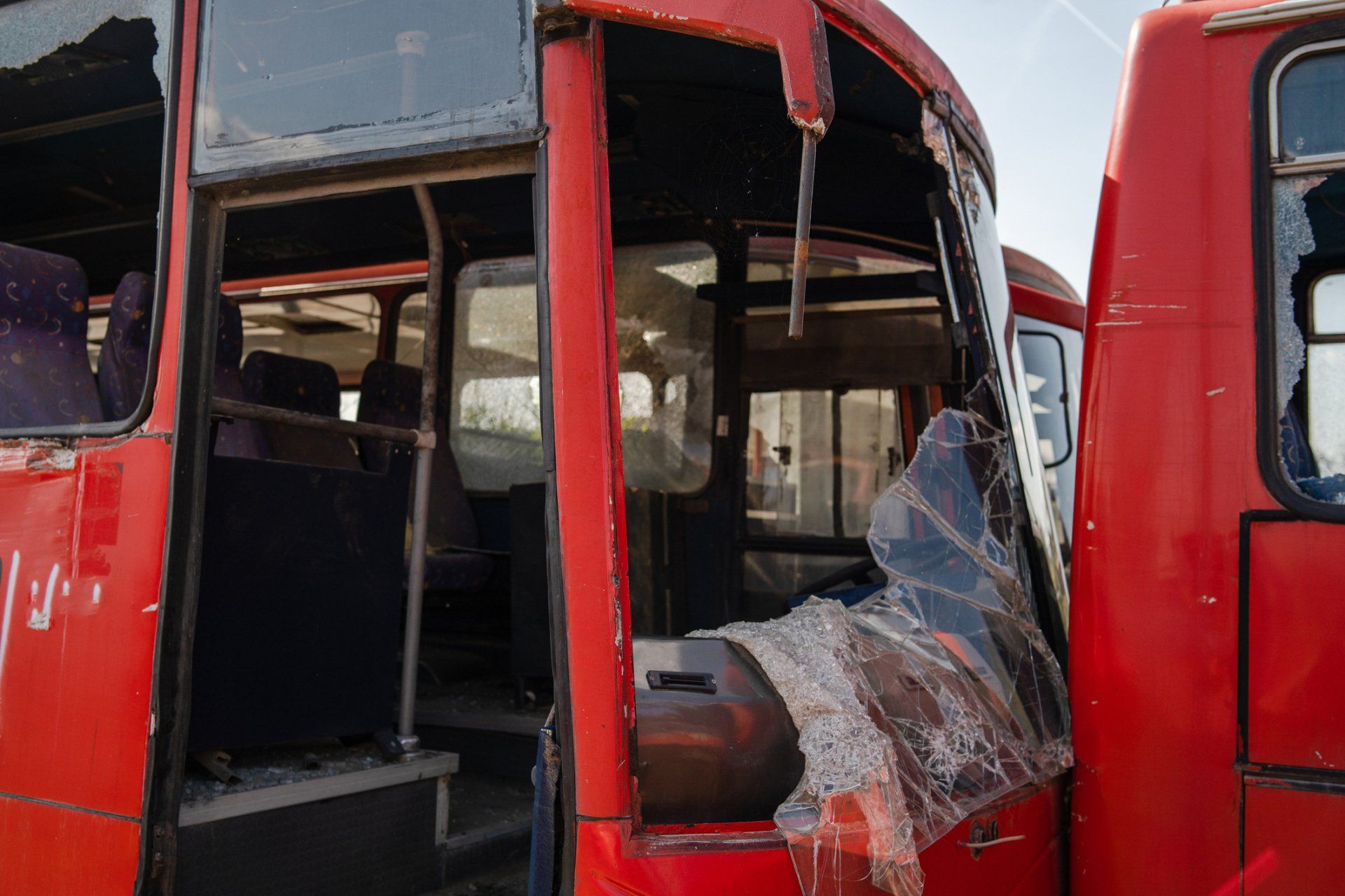 Damaged red buses with shattered windows sit outdoors.